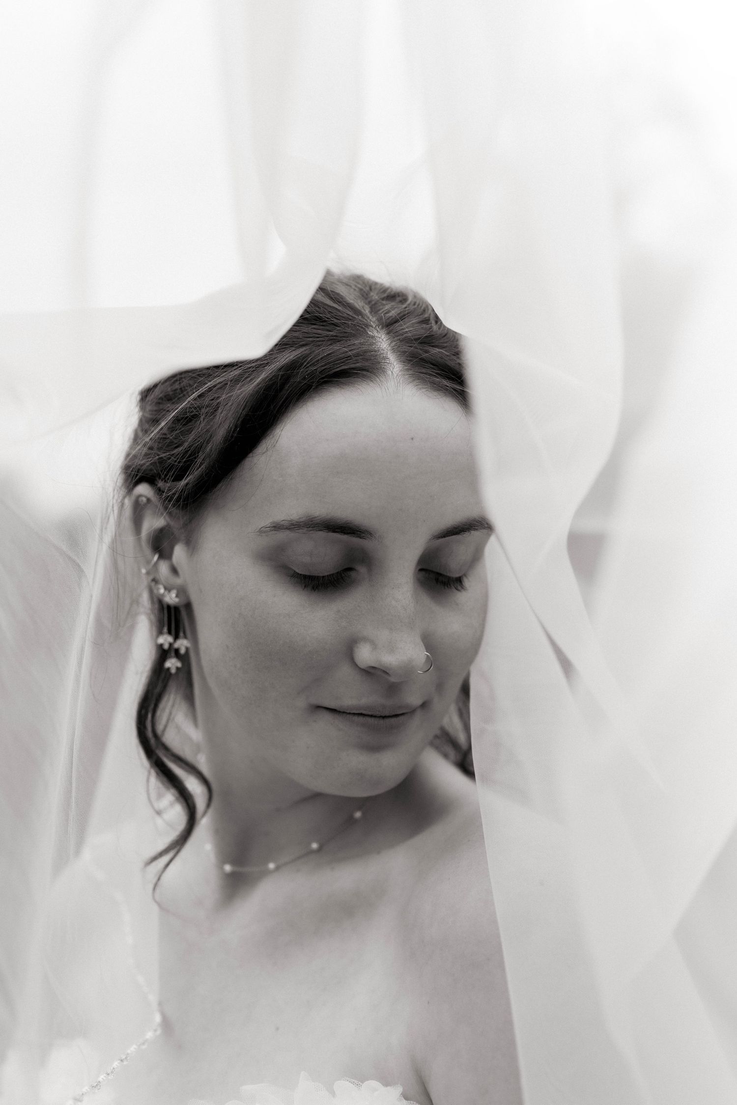Elegant black and white portrait of a bride with eyes closed, draped in a flowing veil wearing pearl earrings. Oklahoma wedding photographer