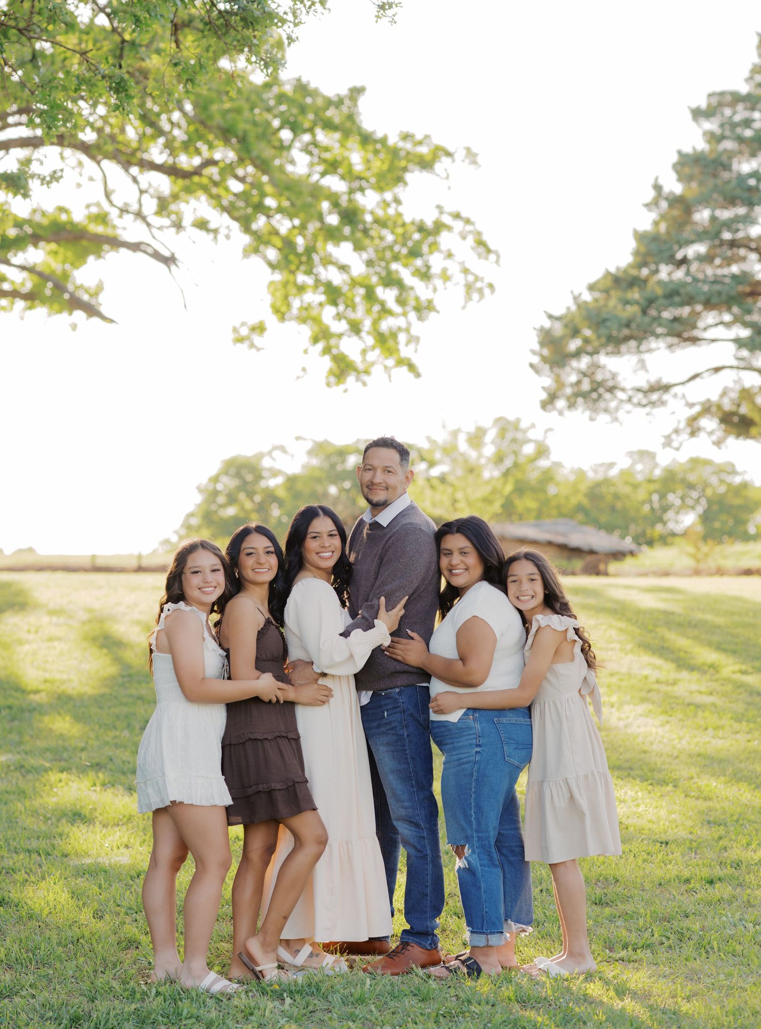 A family of six poses together on a green lawn under a large oak tree during golden hour.