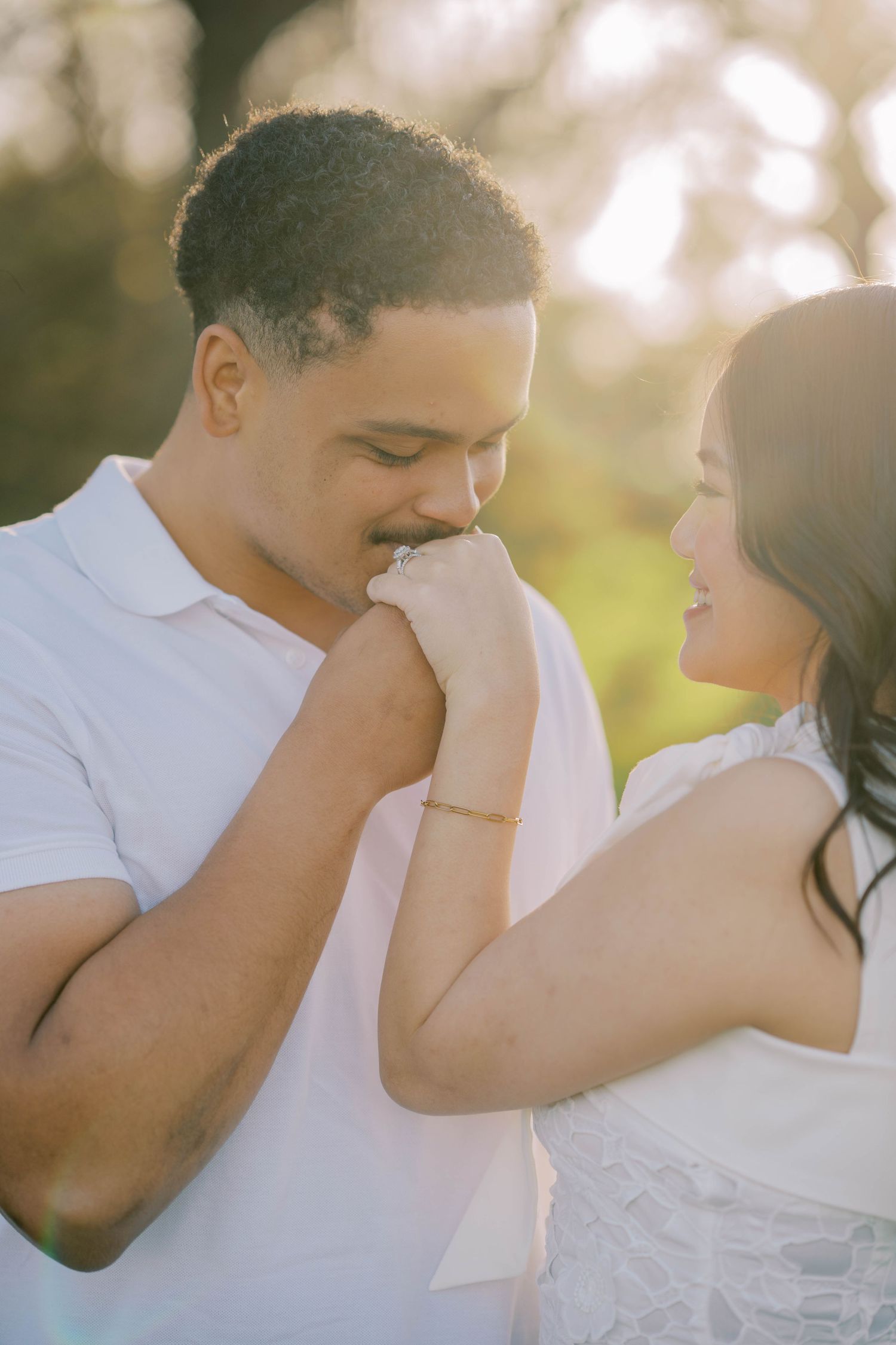 A man gently kisses his partner's hand in a warmly lit outdoor romantic engagement portrait.