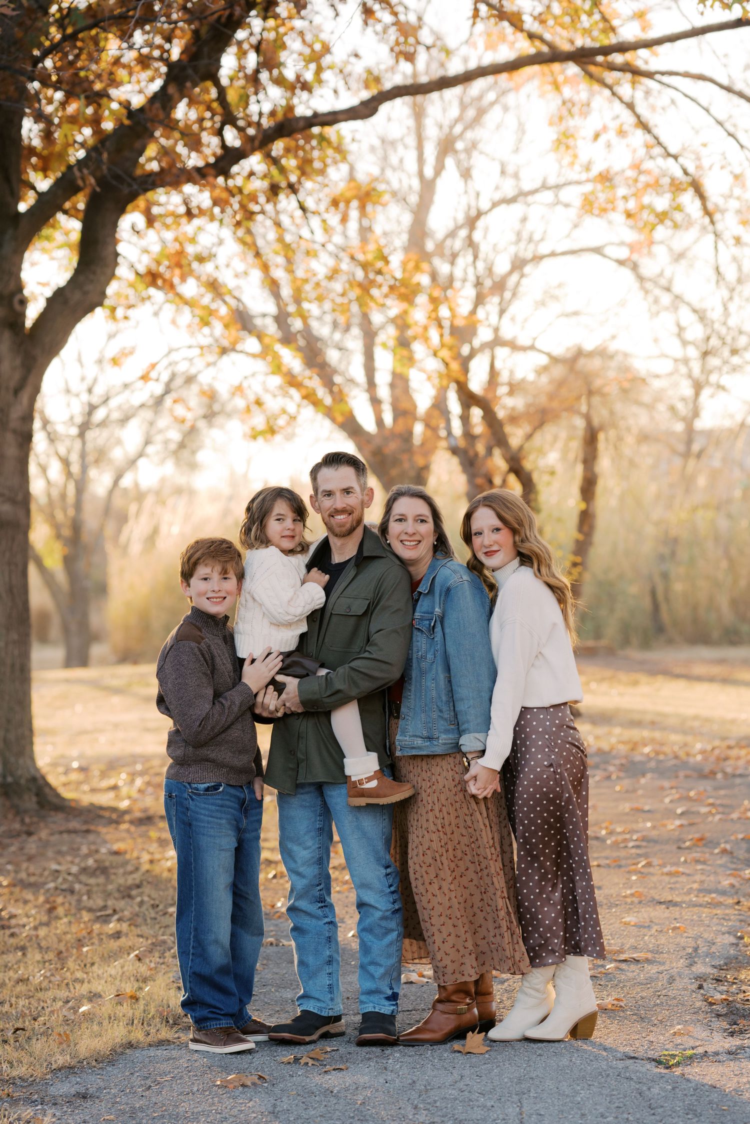 Family of five posing outdoors among autumn trees with golden foliage during a fall portrait session.