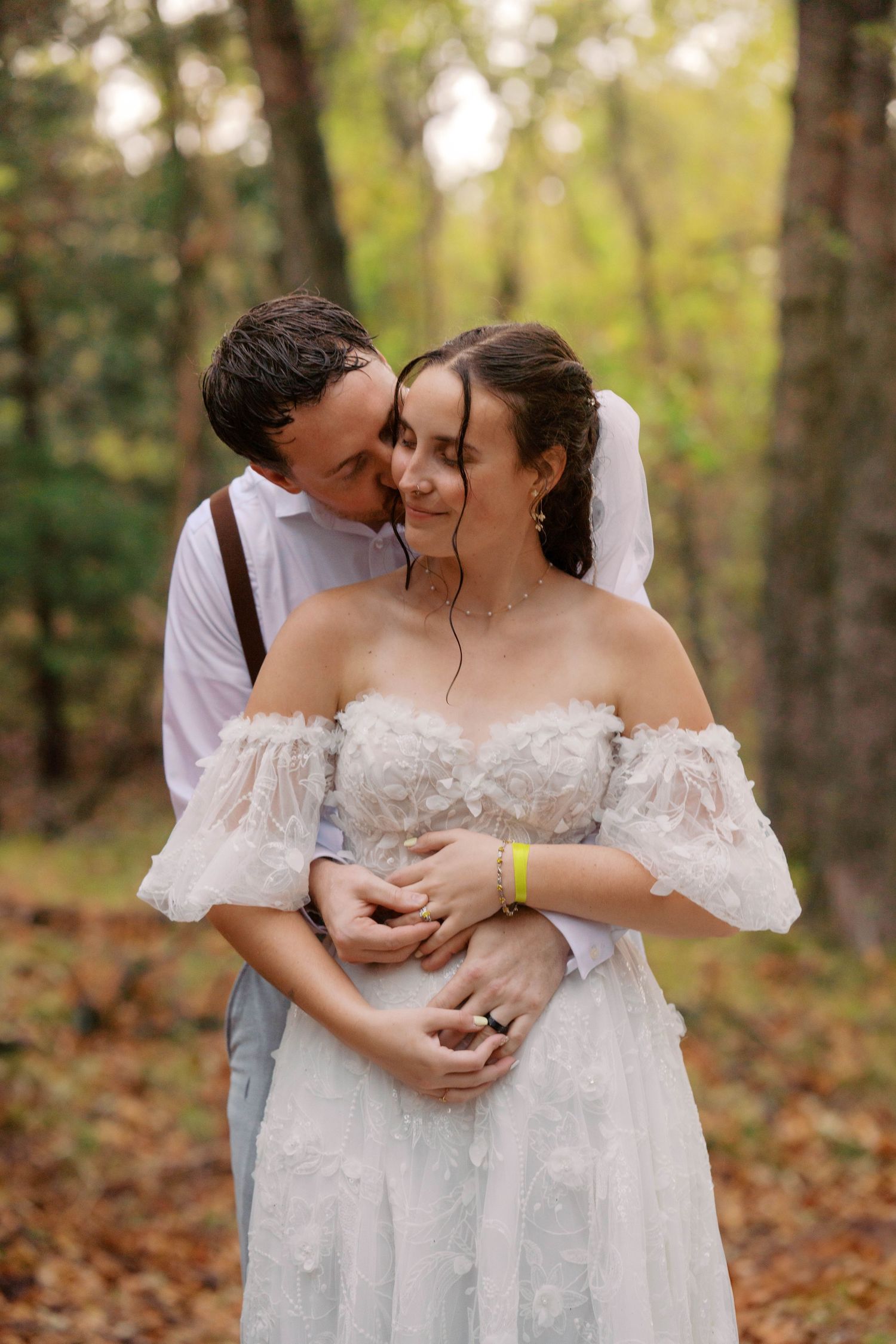 Groom embraces bride from behind in autumn forest, both smiling in romantic wedding portrait. Oklahoma wedding photographer.