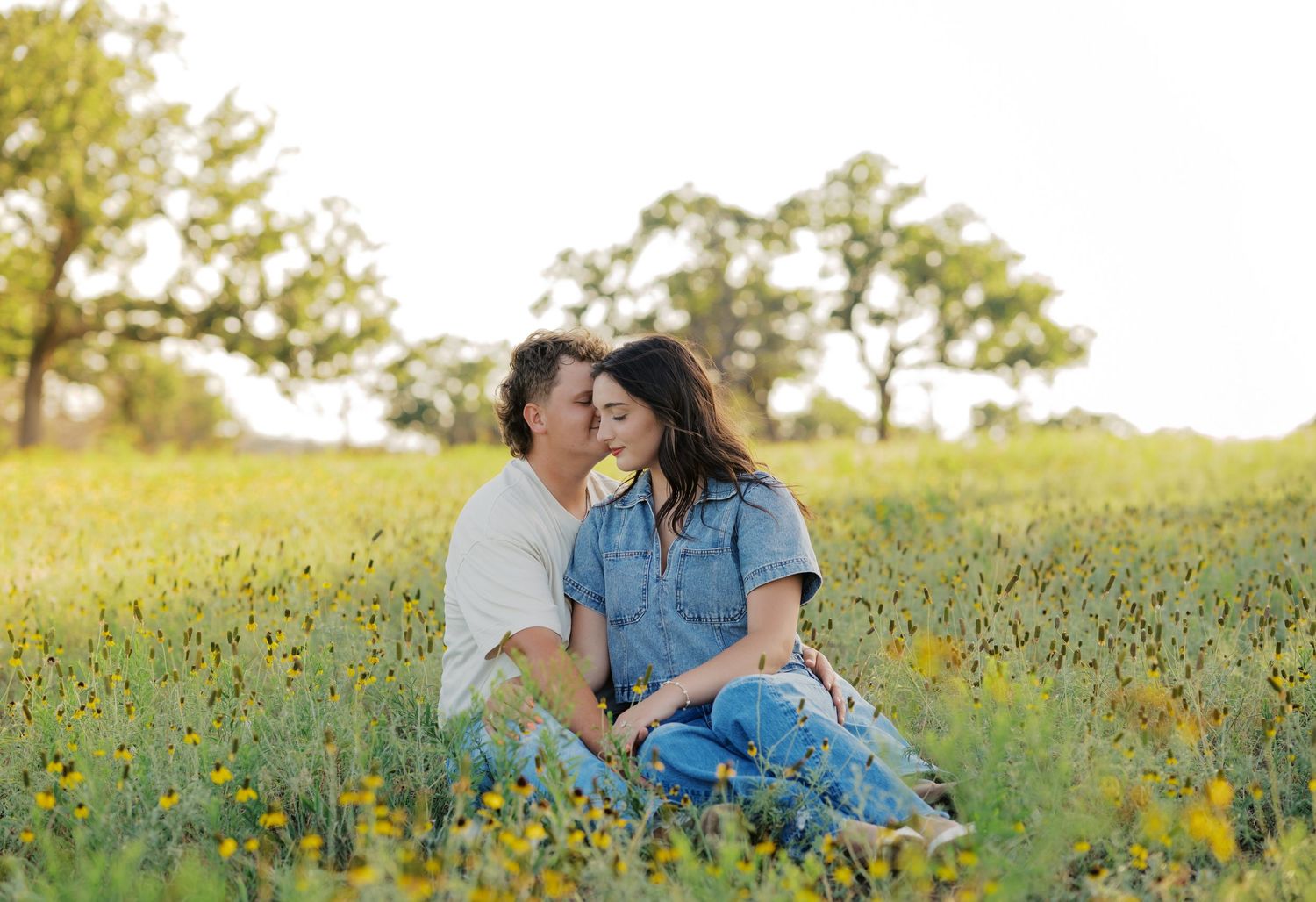 Couple sitting together in a blooming wildflower field during a relaxed Oklahoma engagement session.