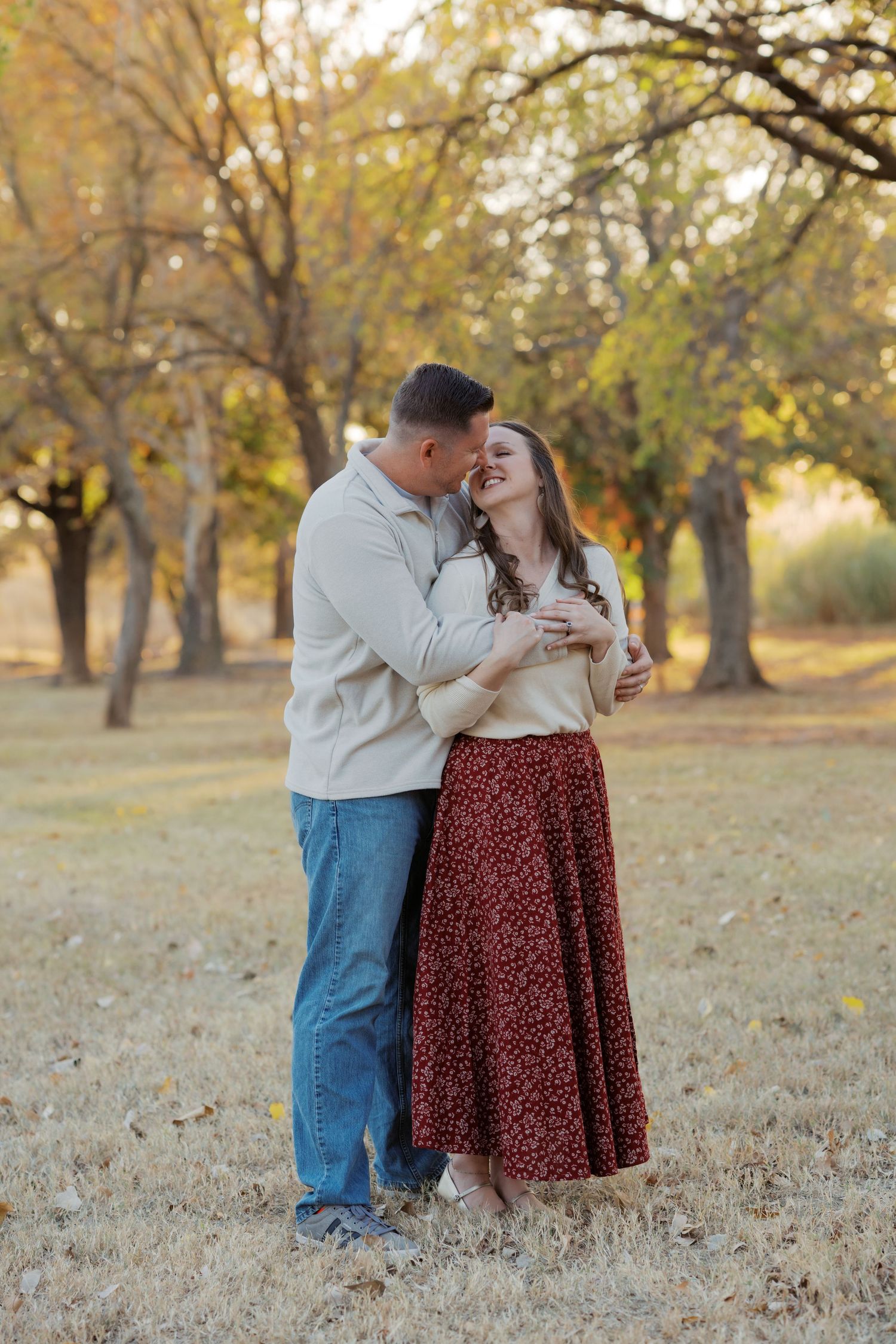 Couple sharing a tender moment laughing together in a golden autumn park with fall foliage.