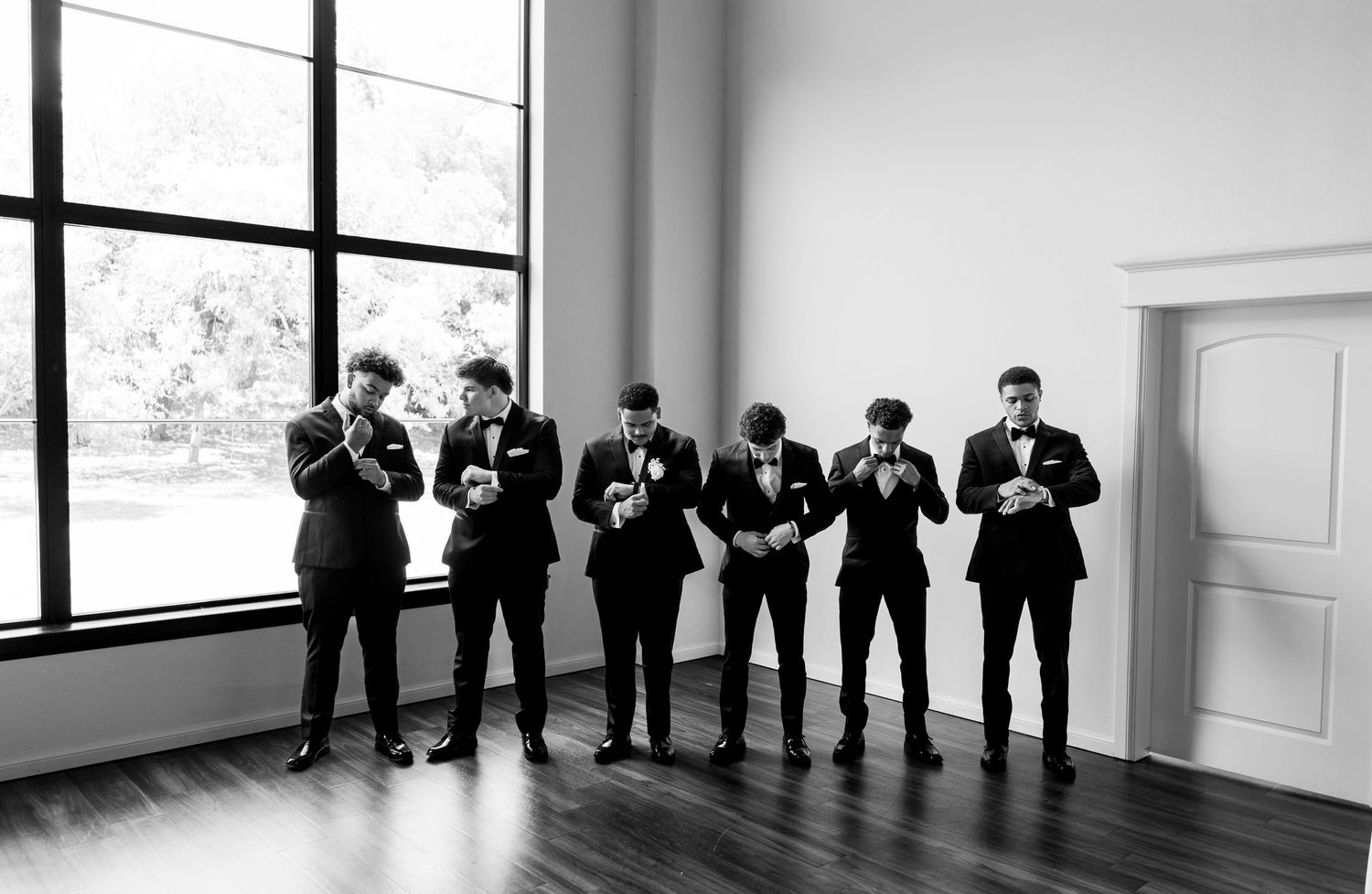 Black and white photo of groomsmen adjusting their boutonnieres before a wedding at Sorelle at Meadow Creek in Oklahoma.