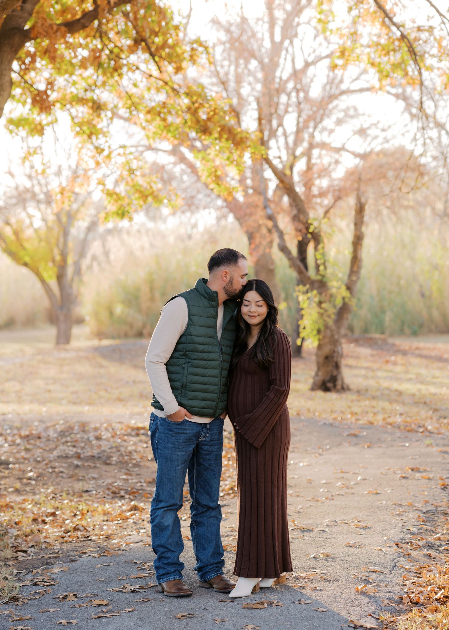 Couple embracing on autumn path surrounded by golden trees during fall engagement photo session.