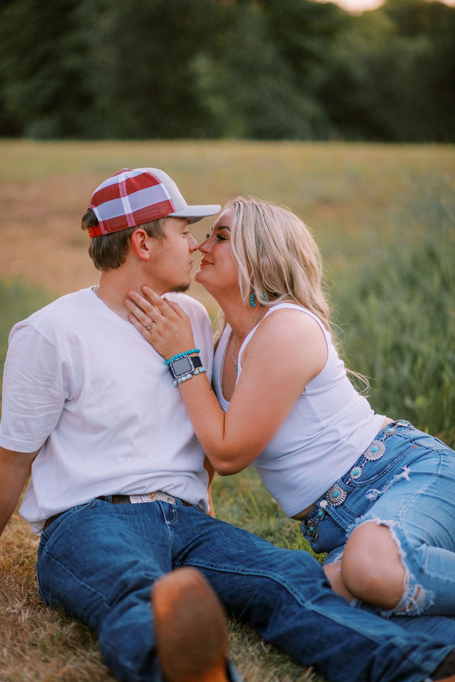 Young couple sharing a kiss while sitting in a sunny green field at golden hour.