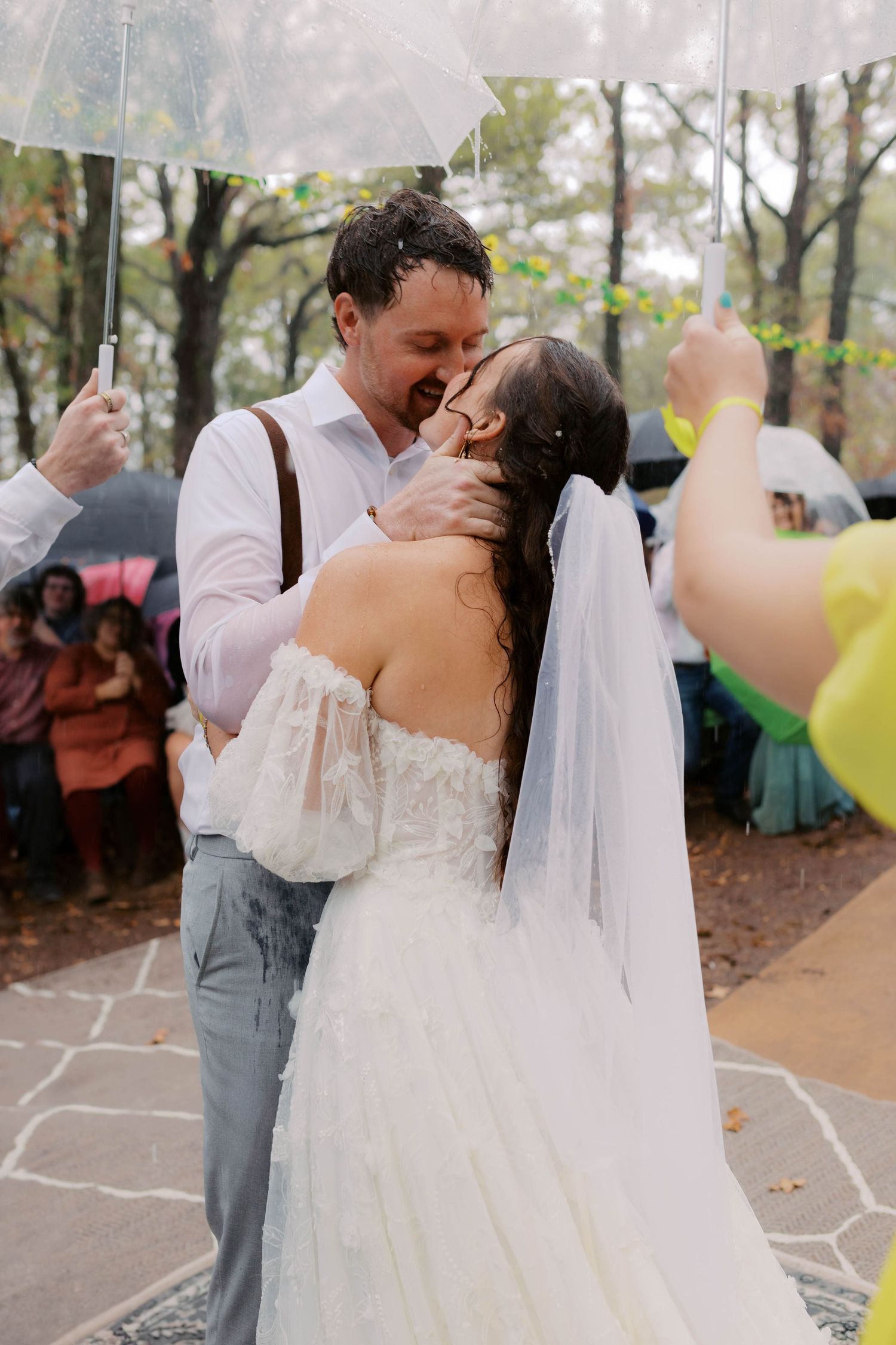 Bride and groom share first kiss in rain under clear umbrella at outdoor wedding ceremony. Oklahoma wedding photographer.