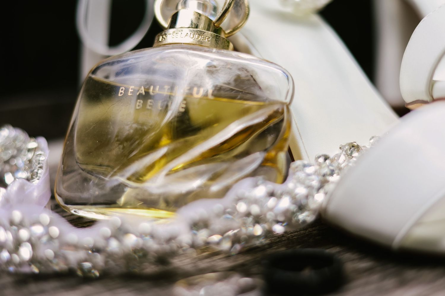 Elegant wedding shoes and perfume bottle arranged with delicate pearl necklaces in a soft white setting.