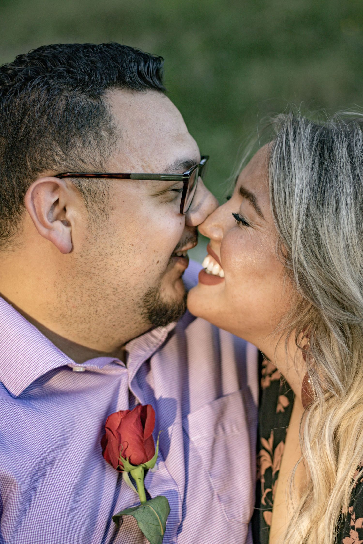 A close-up shot of a couple sharing an intimate moment with a red rose pinned to his shirt.