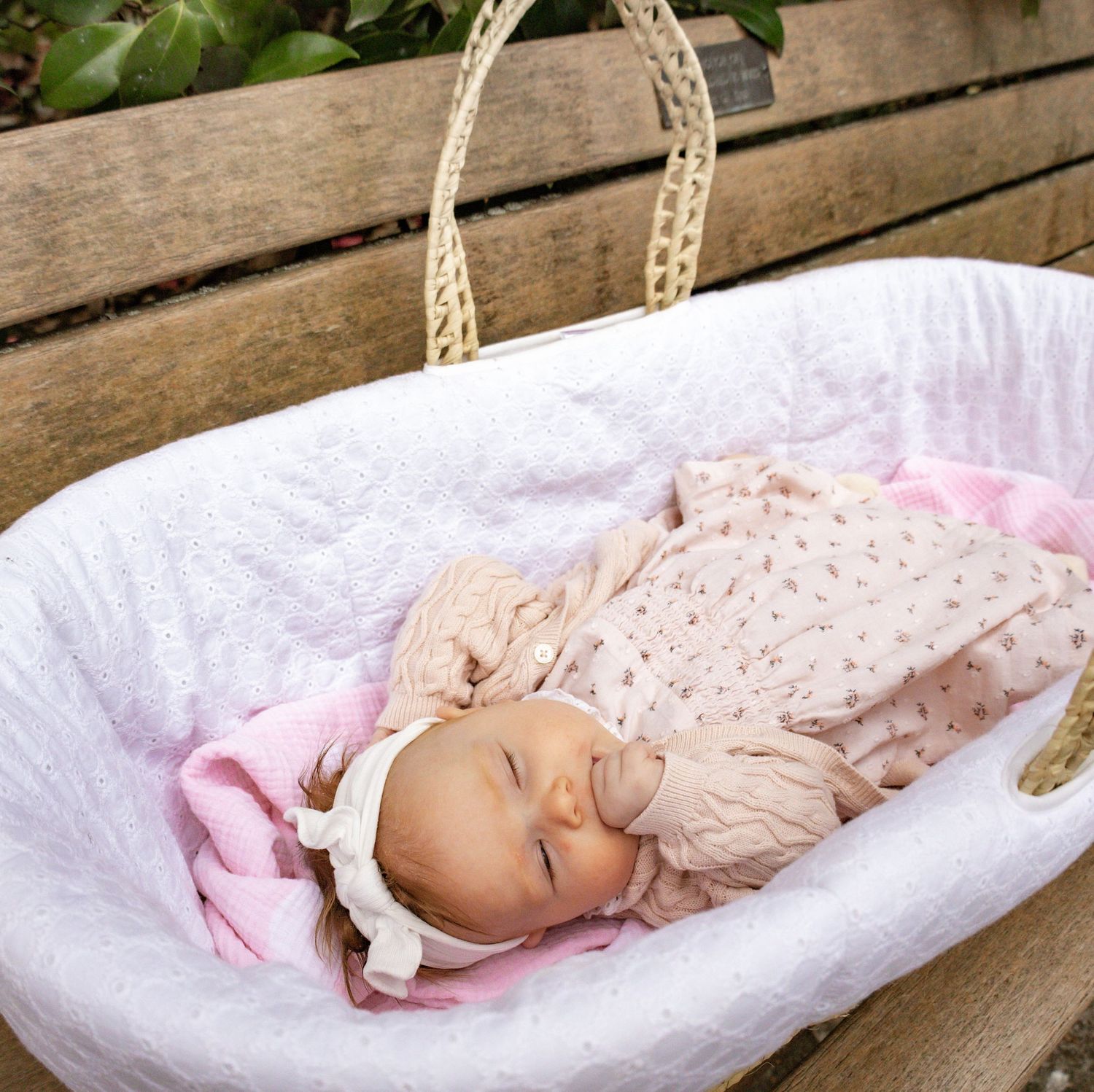A sleeping infant in floral clothing rests in a white bassinet.