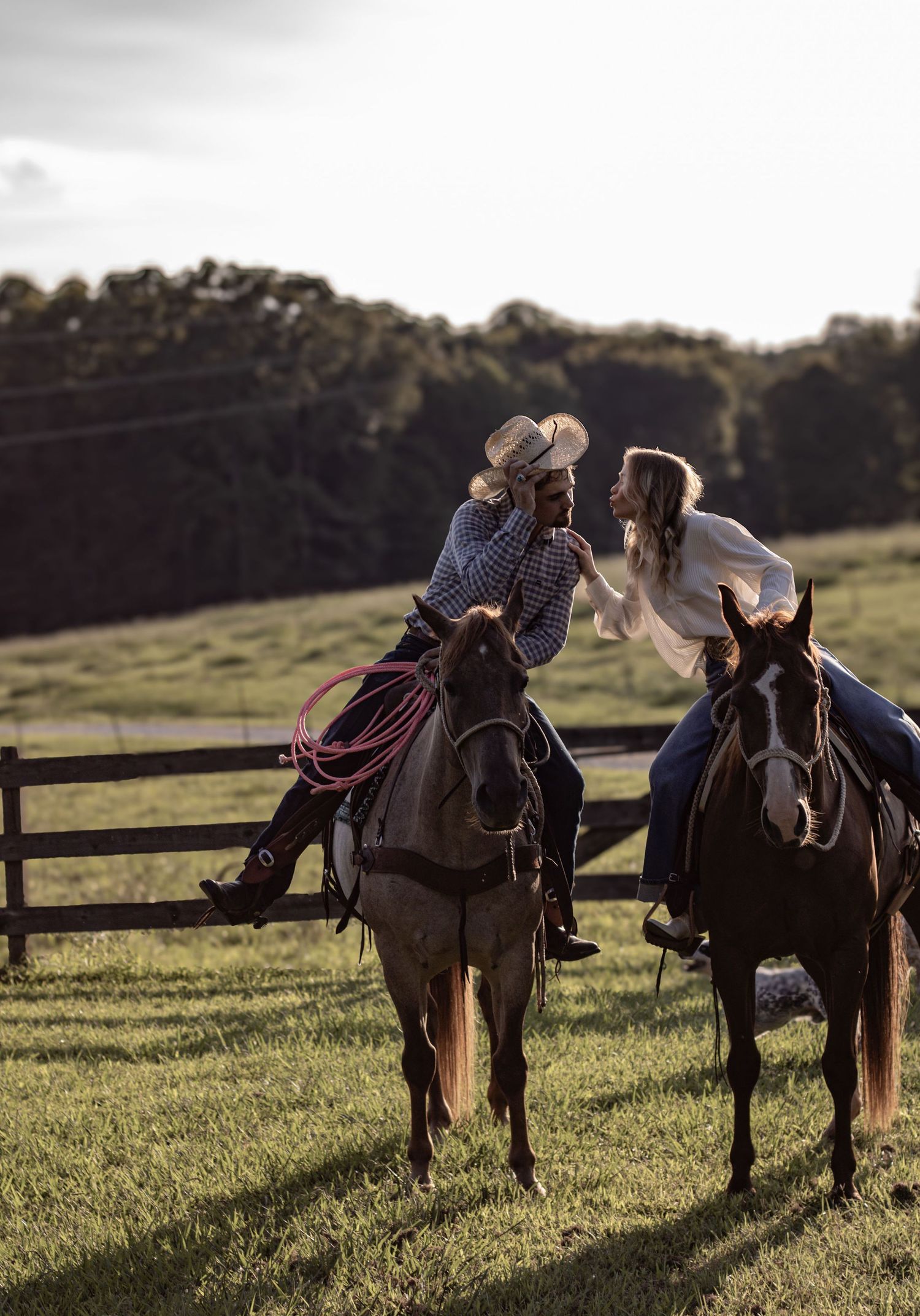 Two people sharing a romantic moment while horseback riding in a pastoral setting.