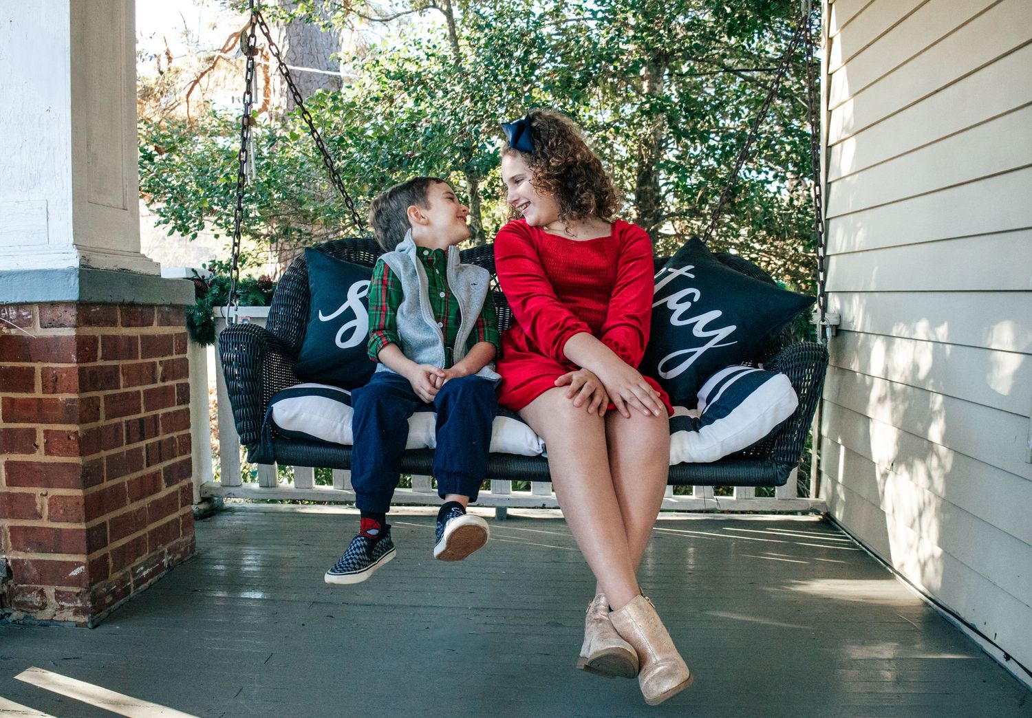 Family sits casually on front porch swing during outdoor photo session.