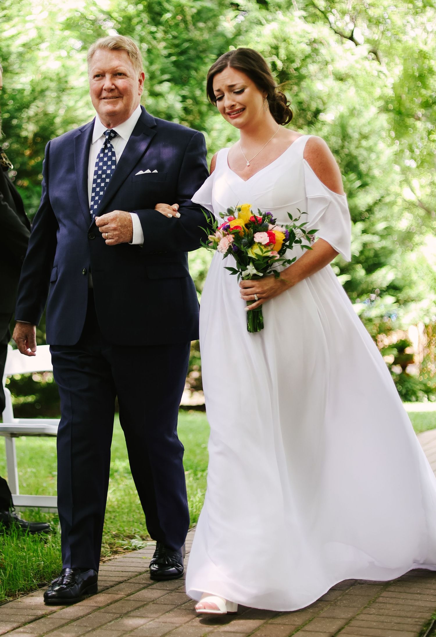 A joyful moment captured at an outdoor wedding ceremony showing a pair walking arm in arm on a wooden deck surrounded by greenery.