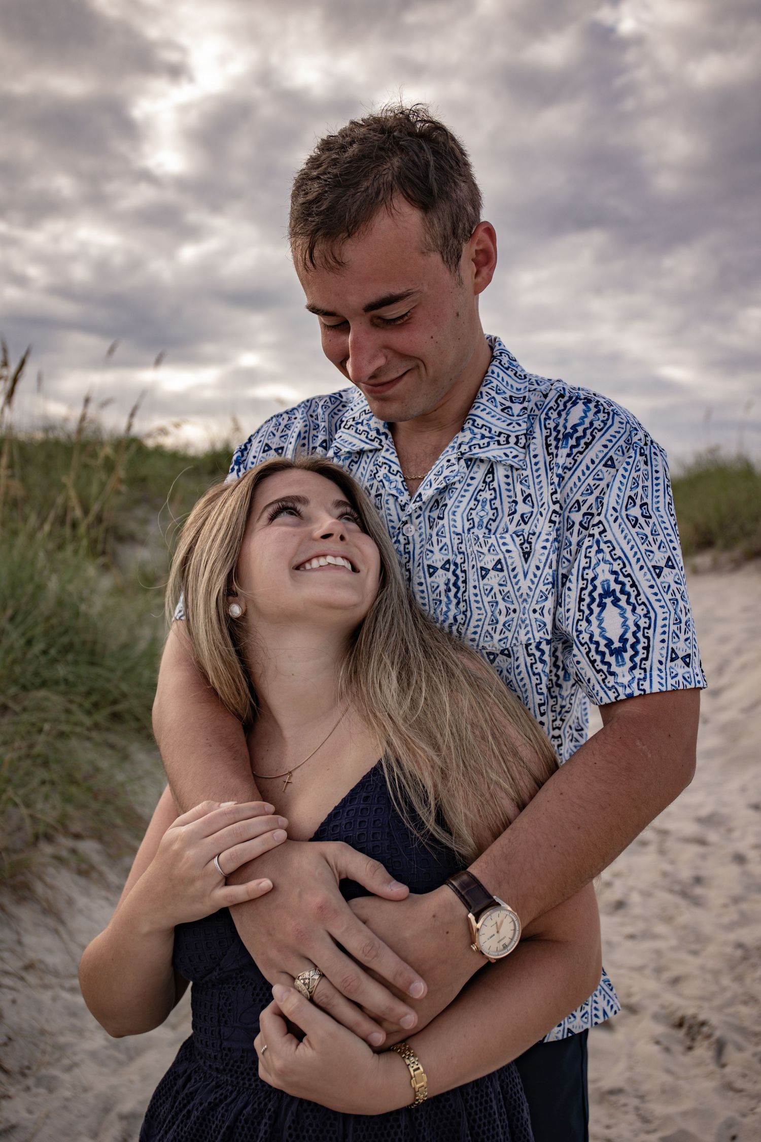 A couple shares intimate moments on a sandy beach under cloudy skies in a series of romantic photos.