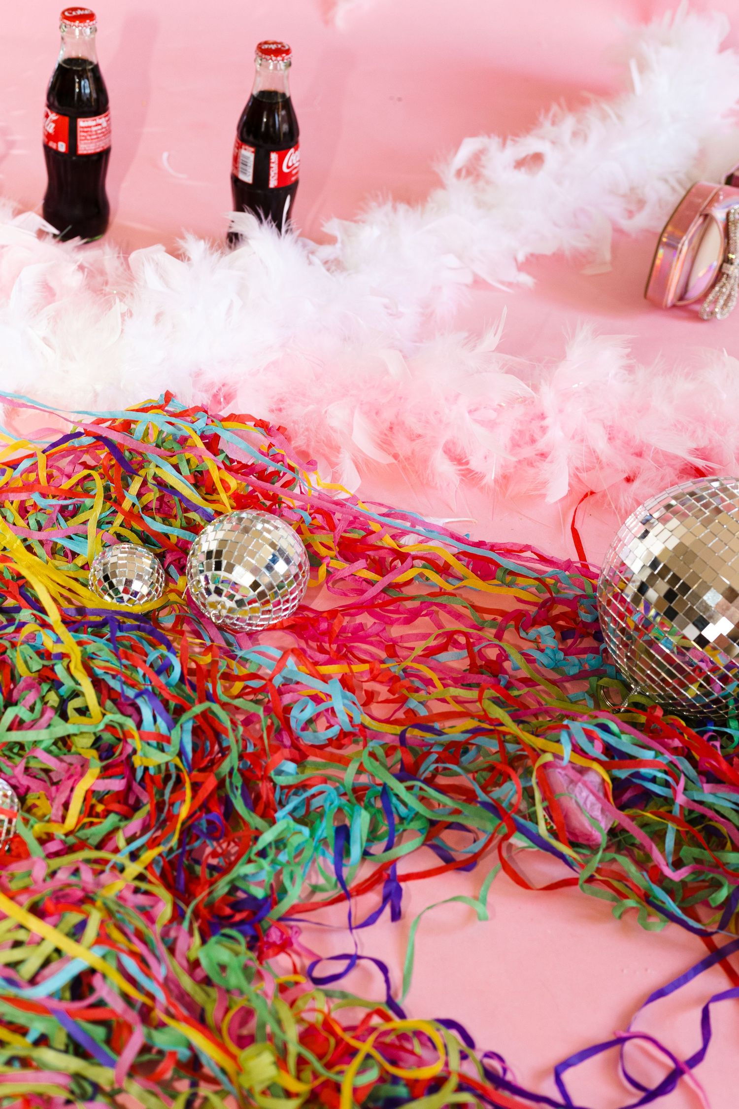 Festive party setup with disco balls, colorful streamers, and Coca-Cola bottles against a pink background.