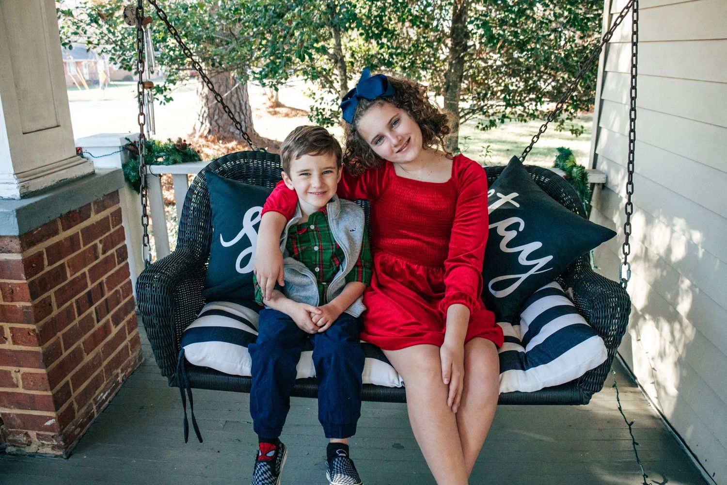 Two people sitting together on a porch swing with dark cushions on a sunny day.