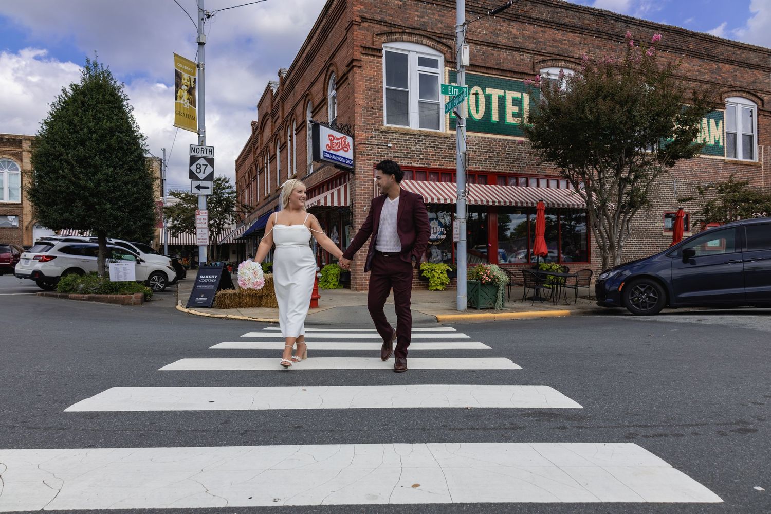 A couple crosses a city street in front of a historic brick hotel building.