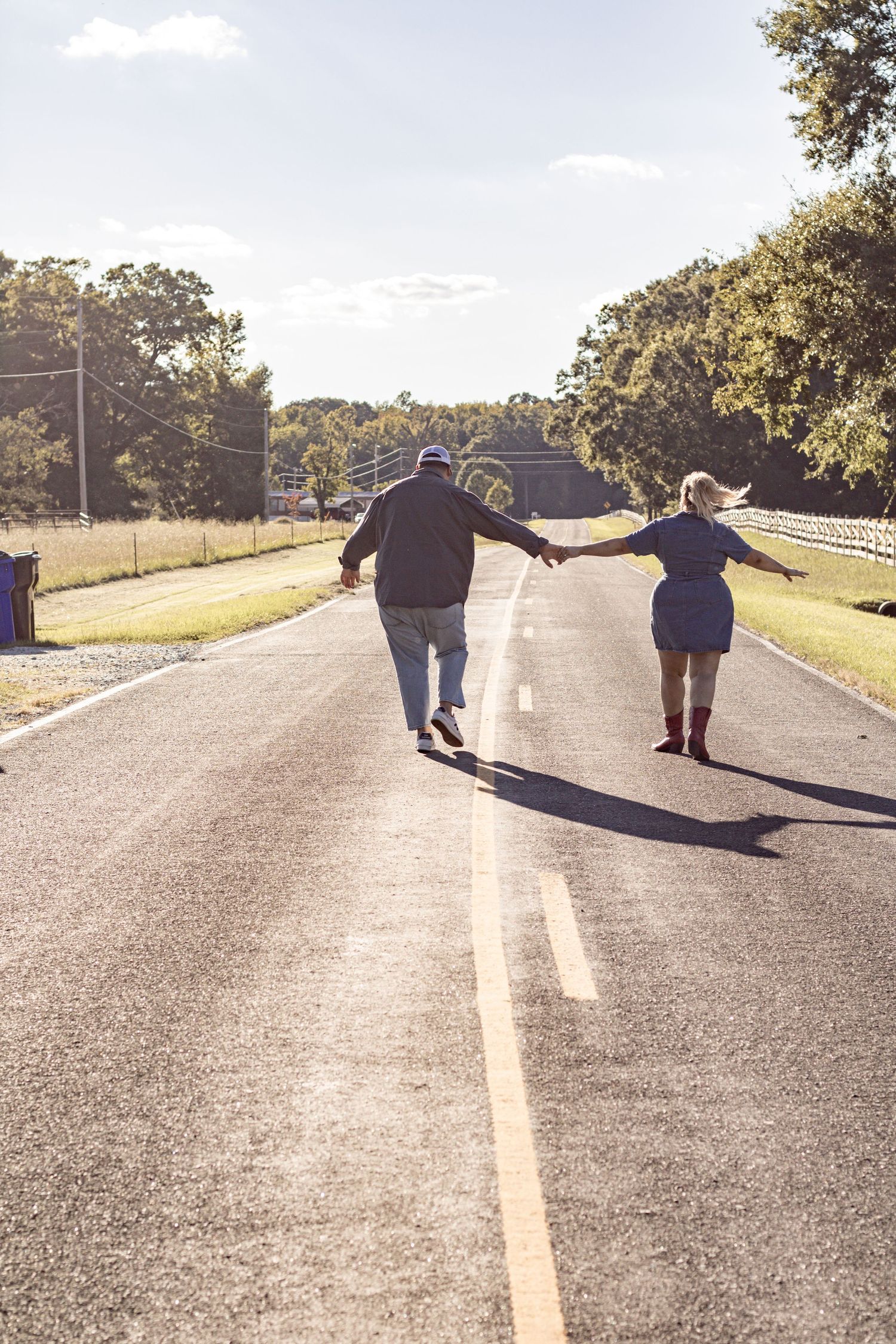 Couple walking hand in hand down empty rural road at sunset.