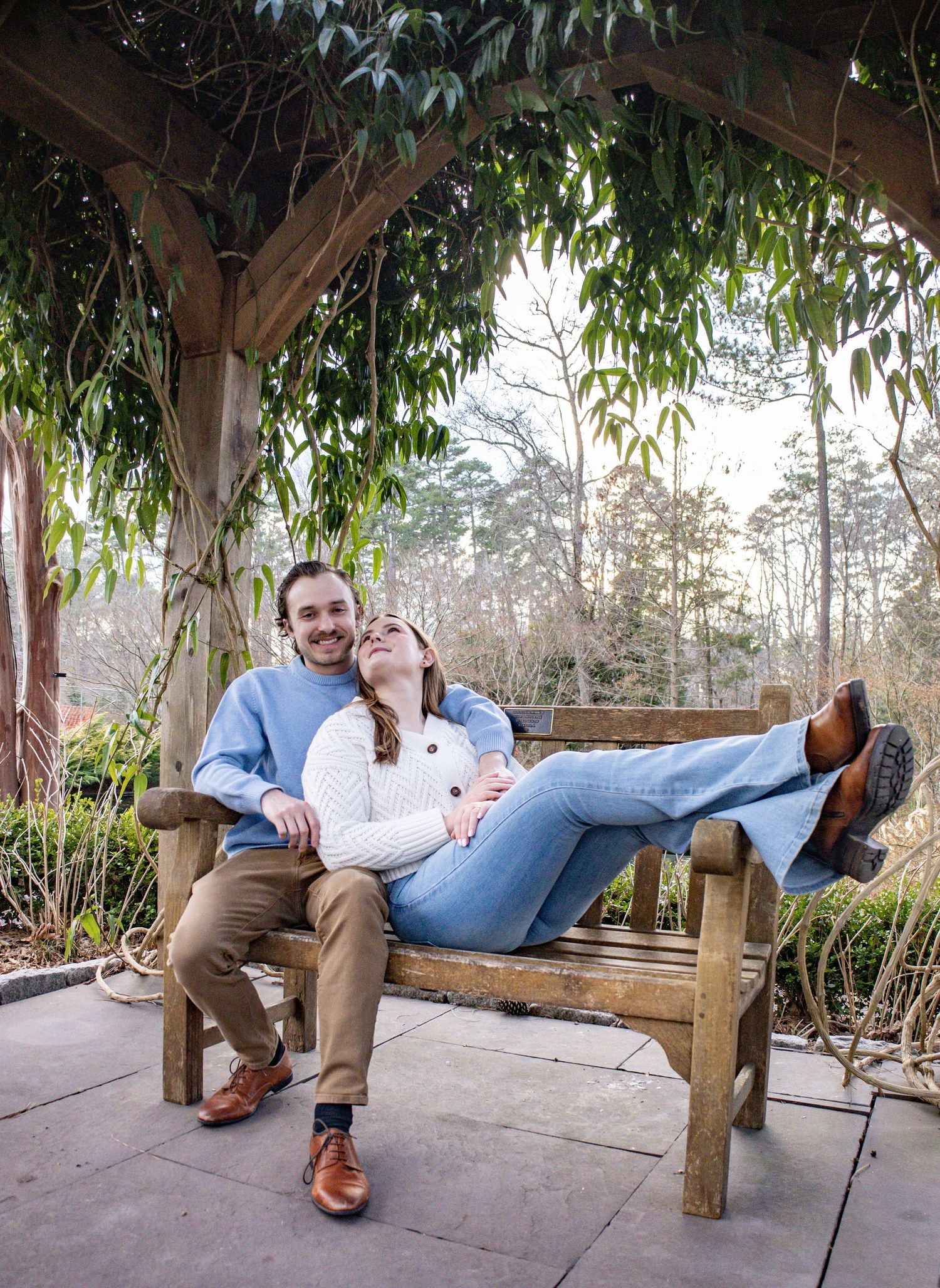 Couple relaxes together on wooden bench in garden setting.