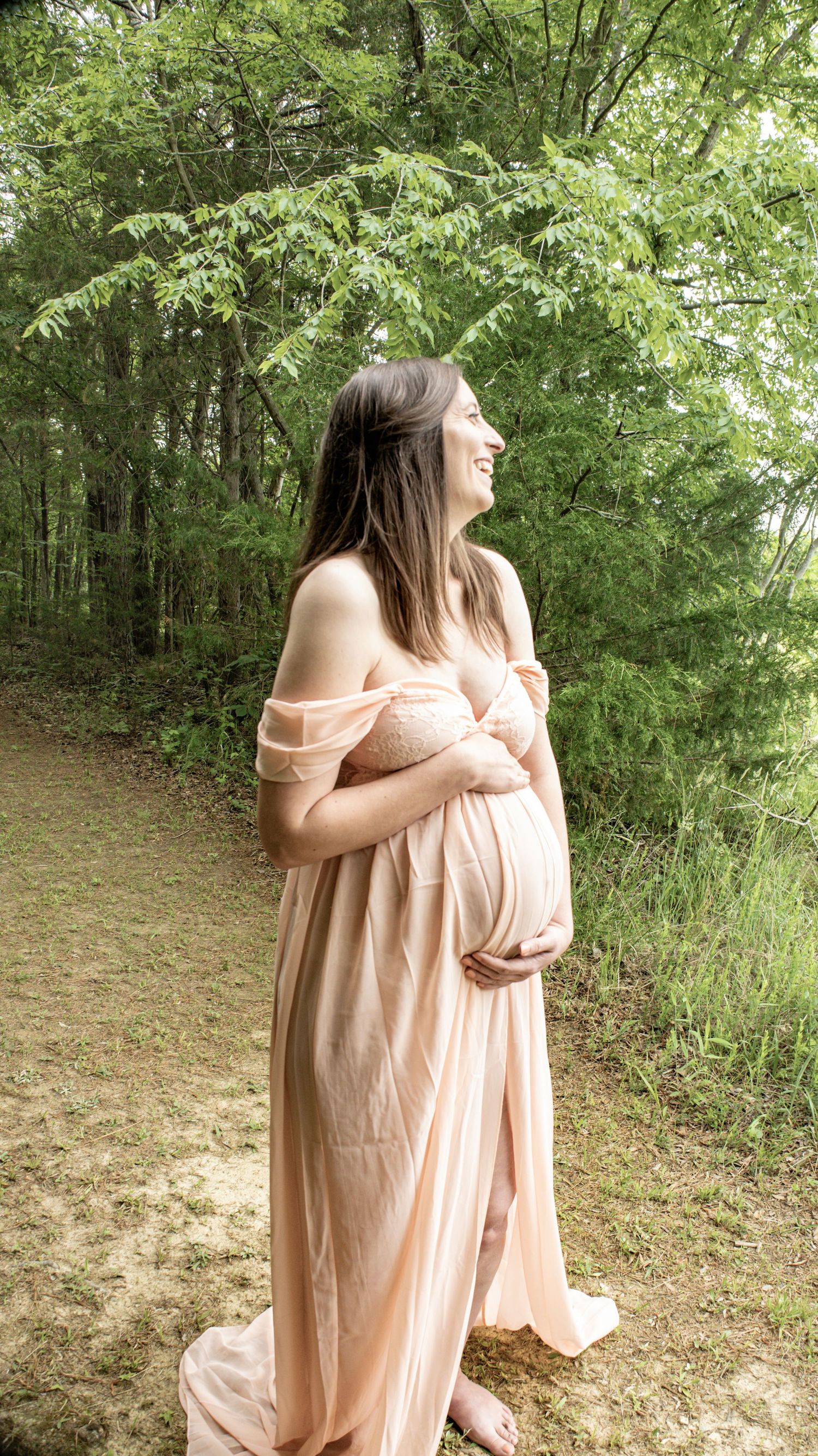 A person in a blush-colored dress poses against lush green foliage.