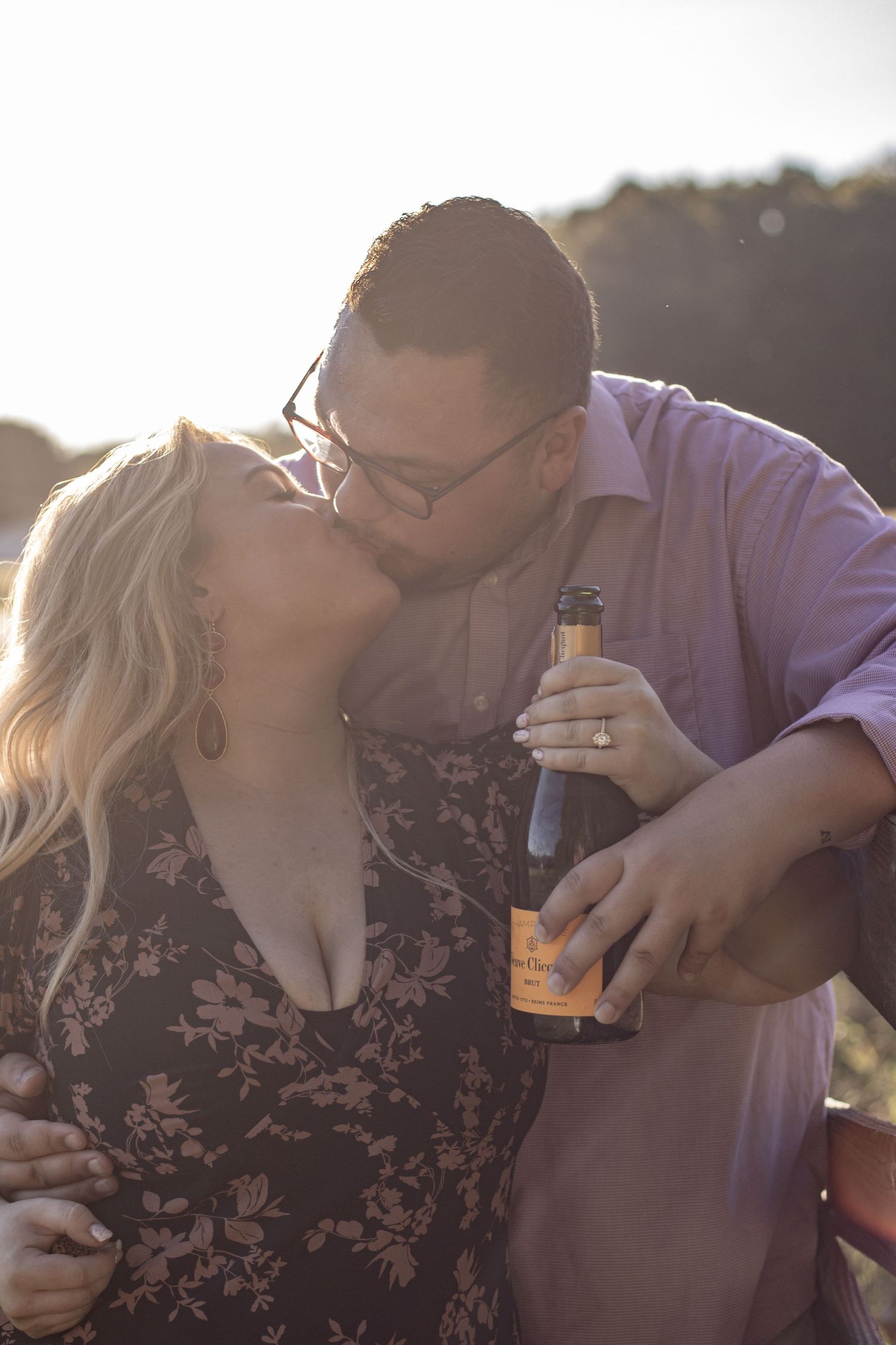 Romantic couple sharing intimate moment while holding champagne bottle in golden sunlight.