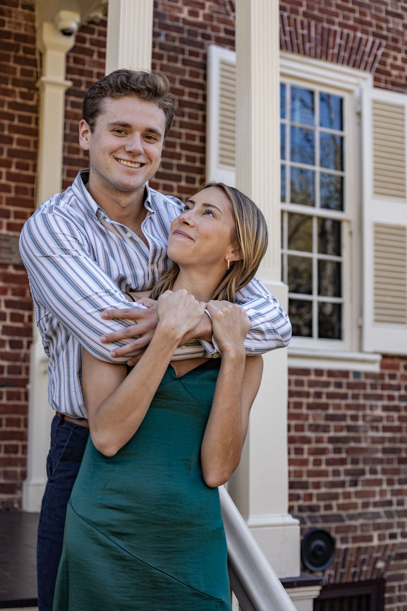 A couple embracing on the steps of a historic brick building with white columns.