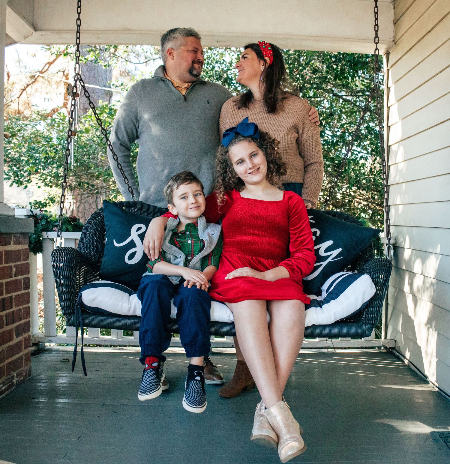 Relaxed family portrait on porch swing with natural lighting and brick accents.