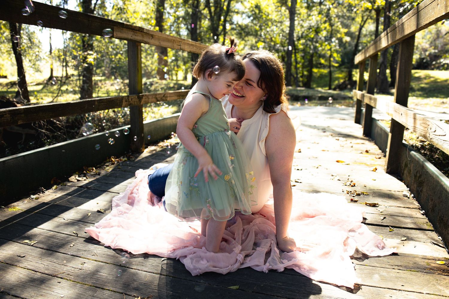 Soft sunlight streams through trees onto a rustic wooden bridge during an outdoor photo session.