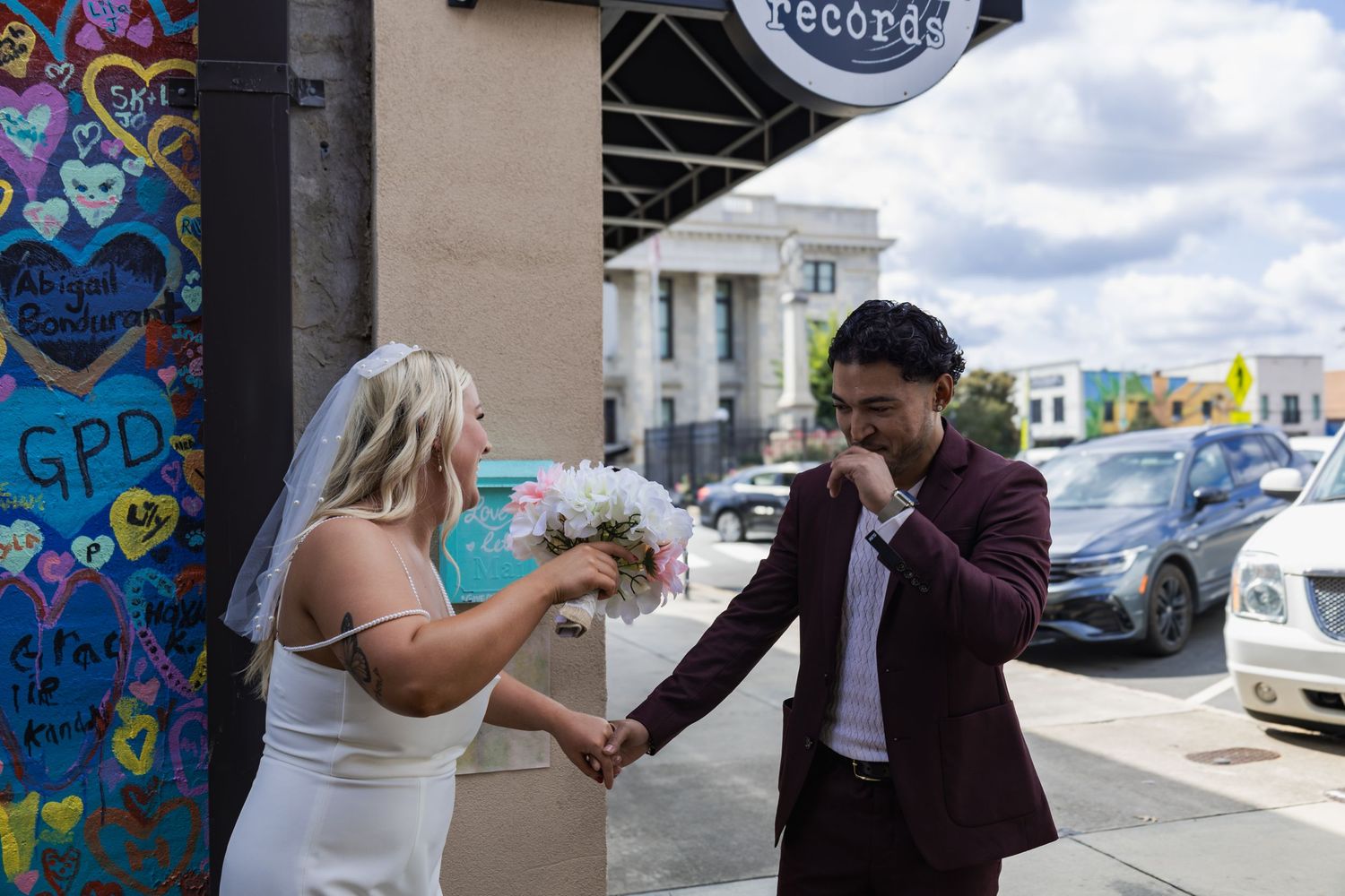 A couple shares a joyful moment outside a storefront with colorful graffiti in the background.