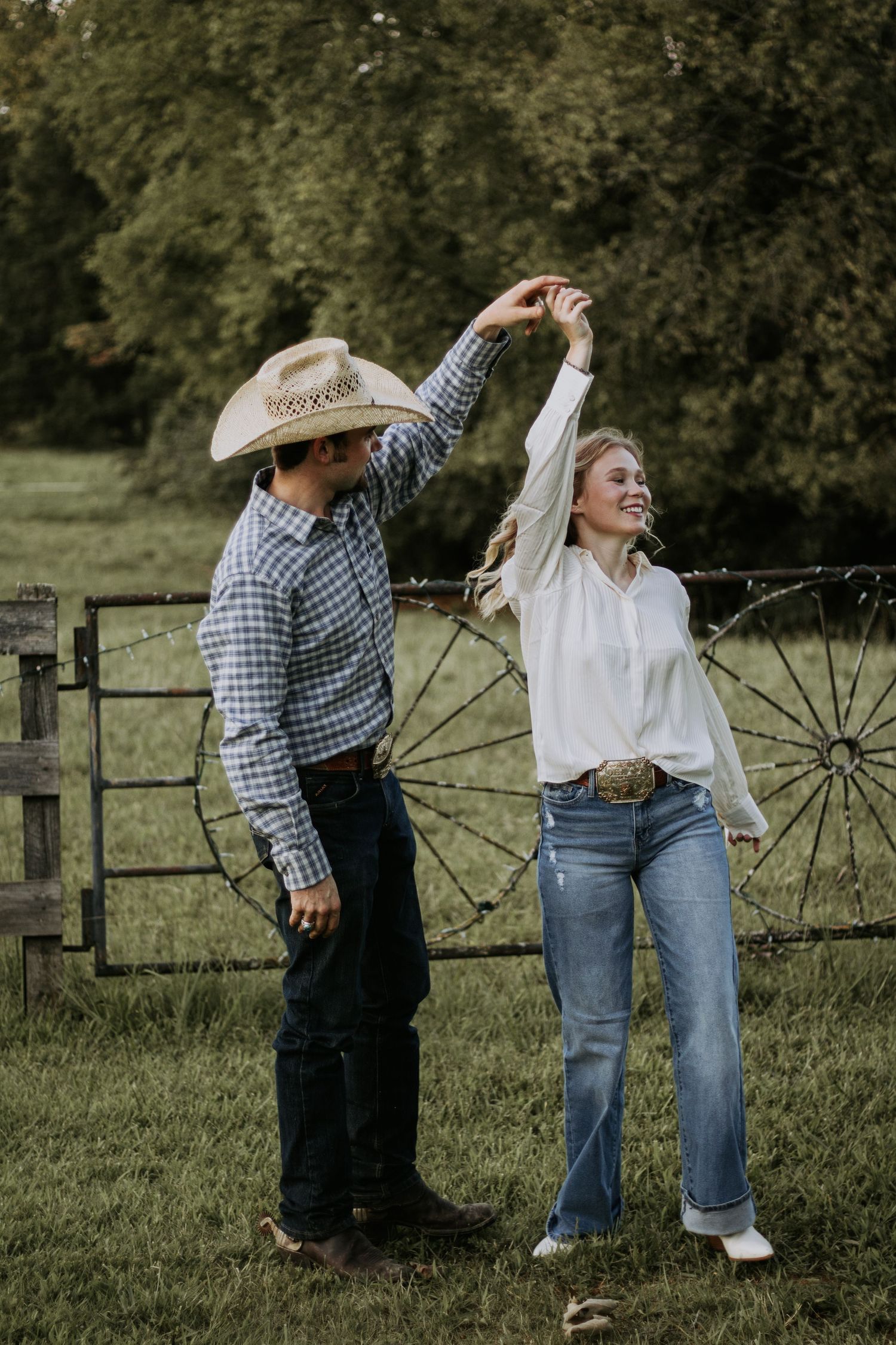 A couple dancing and twirling in a rustic country setting with an old wagon wheel.