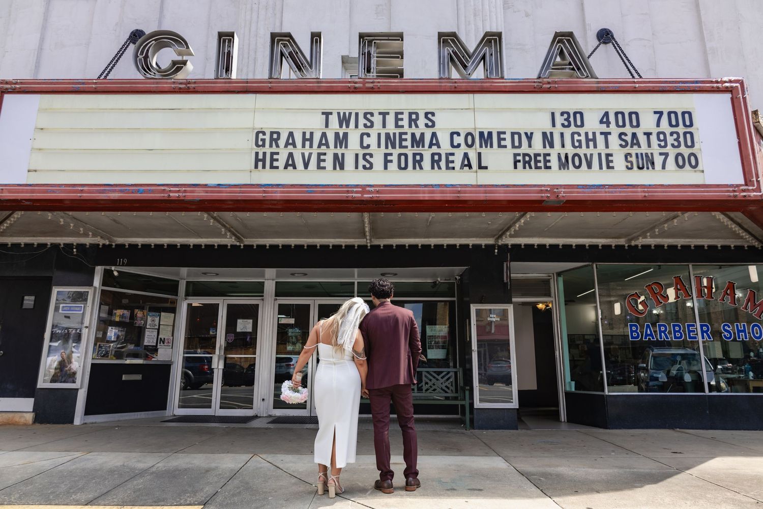 A couple stands outside a vintage cinema theater with movie titles displayed on the marquee.