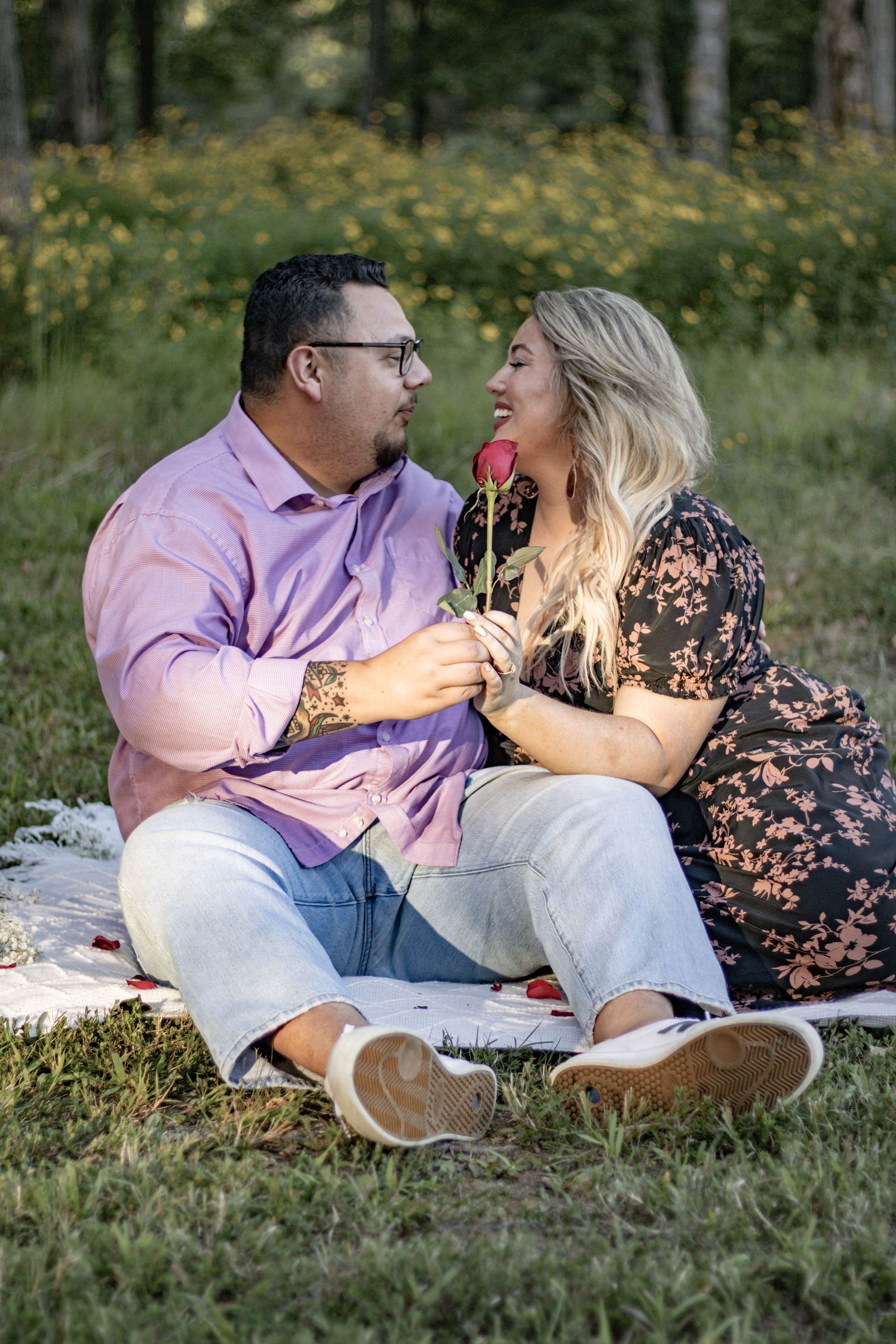 A couple shares a playful moment with a red rose during their romantic picnic.