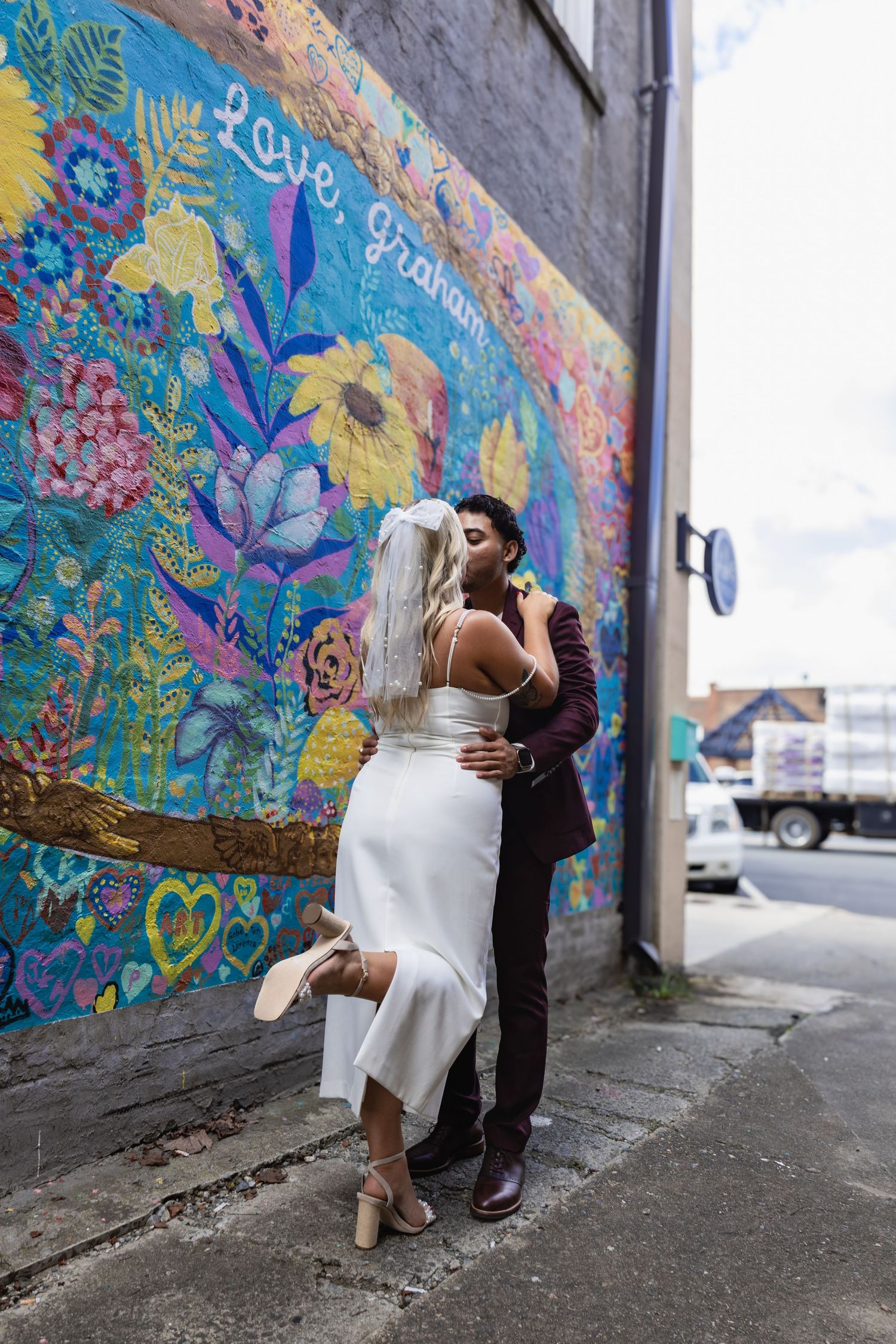 A couple shares an intimate dance moment in front of a painted floral wall.