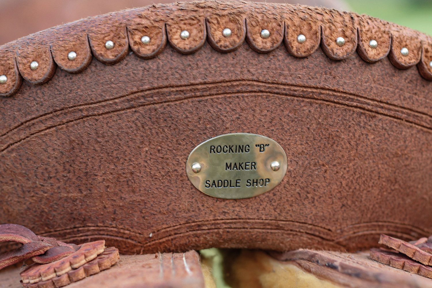 Detailed view of studded trim and maker's plate on brown leather saddle.
