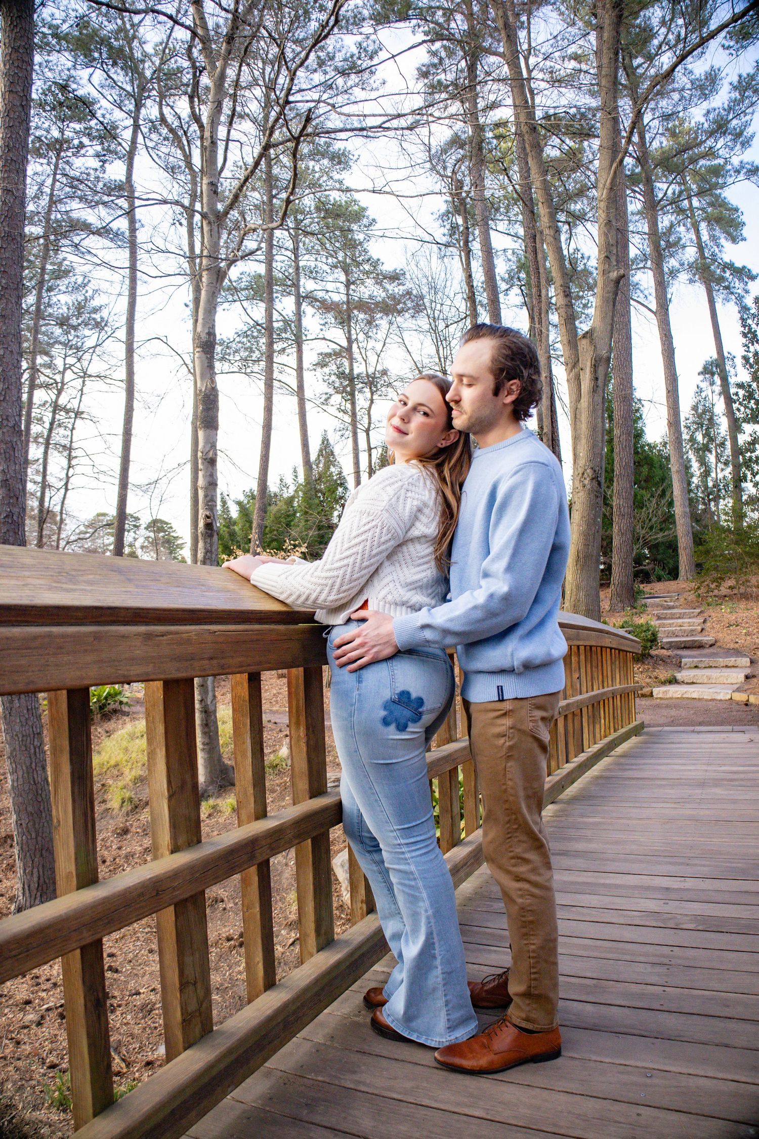 Romantic sequence on wooden boardwalk surrounded by tall pine trees.