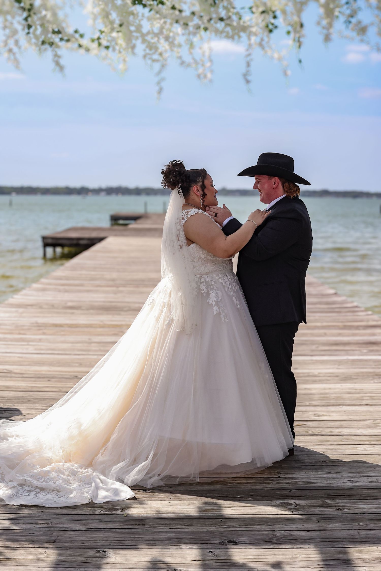 A romantic wedding ceremony takes place on a wooden dock overlooking a serene lake under flowering branches.