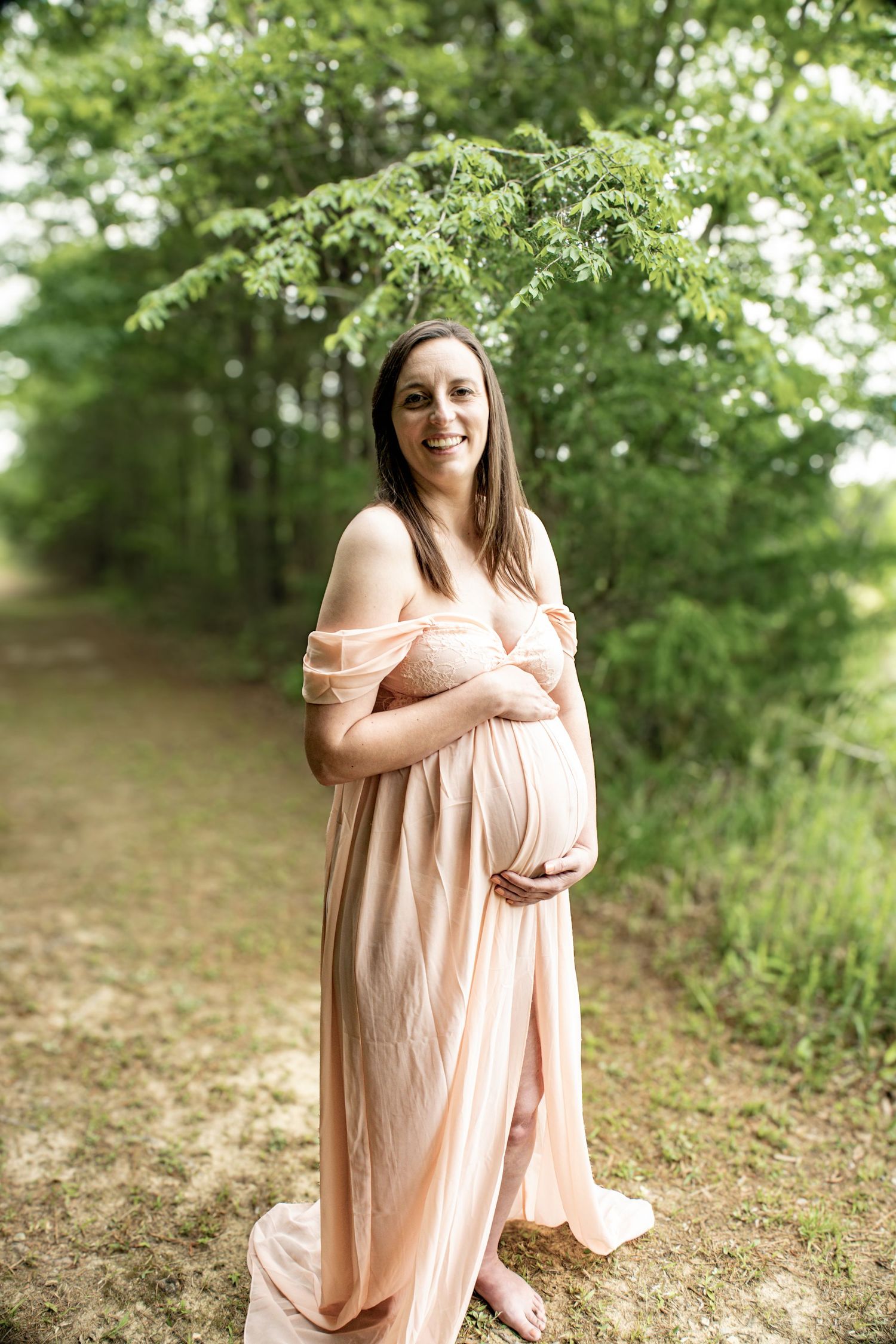Radiant pregnant woman in peach gown poses during forest maternity session.