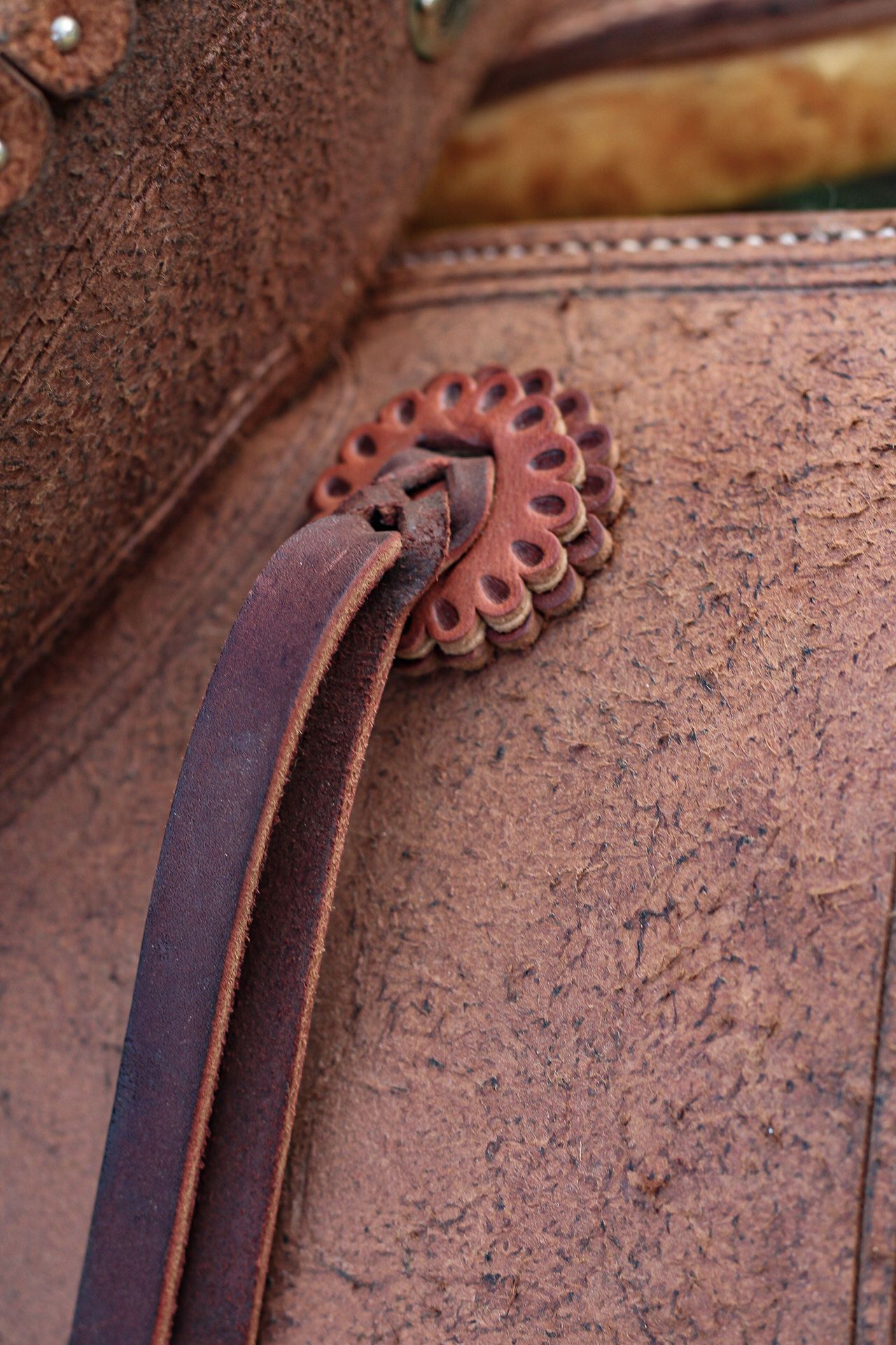 Decorative leather strap threading through an ornate concho on a western saddle.