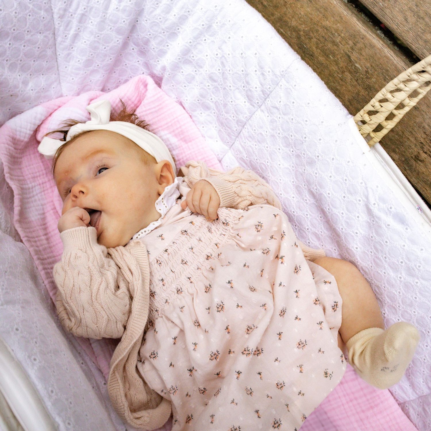 A sleeping baby wearing a pink floral outfit on white bedding.