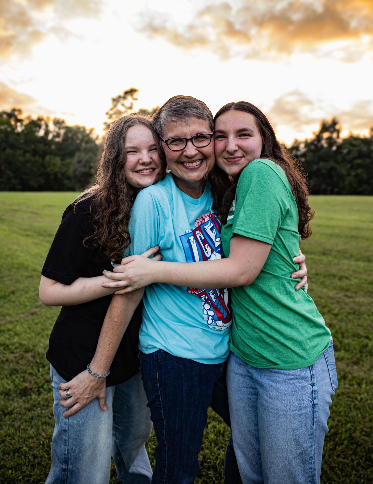 A group embraces while laughing together in a grassy field during golden hour sunset.