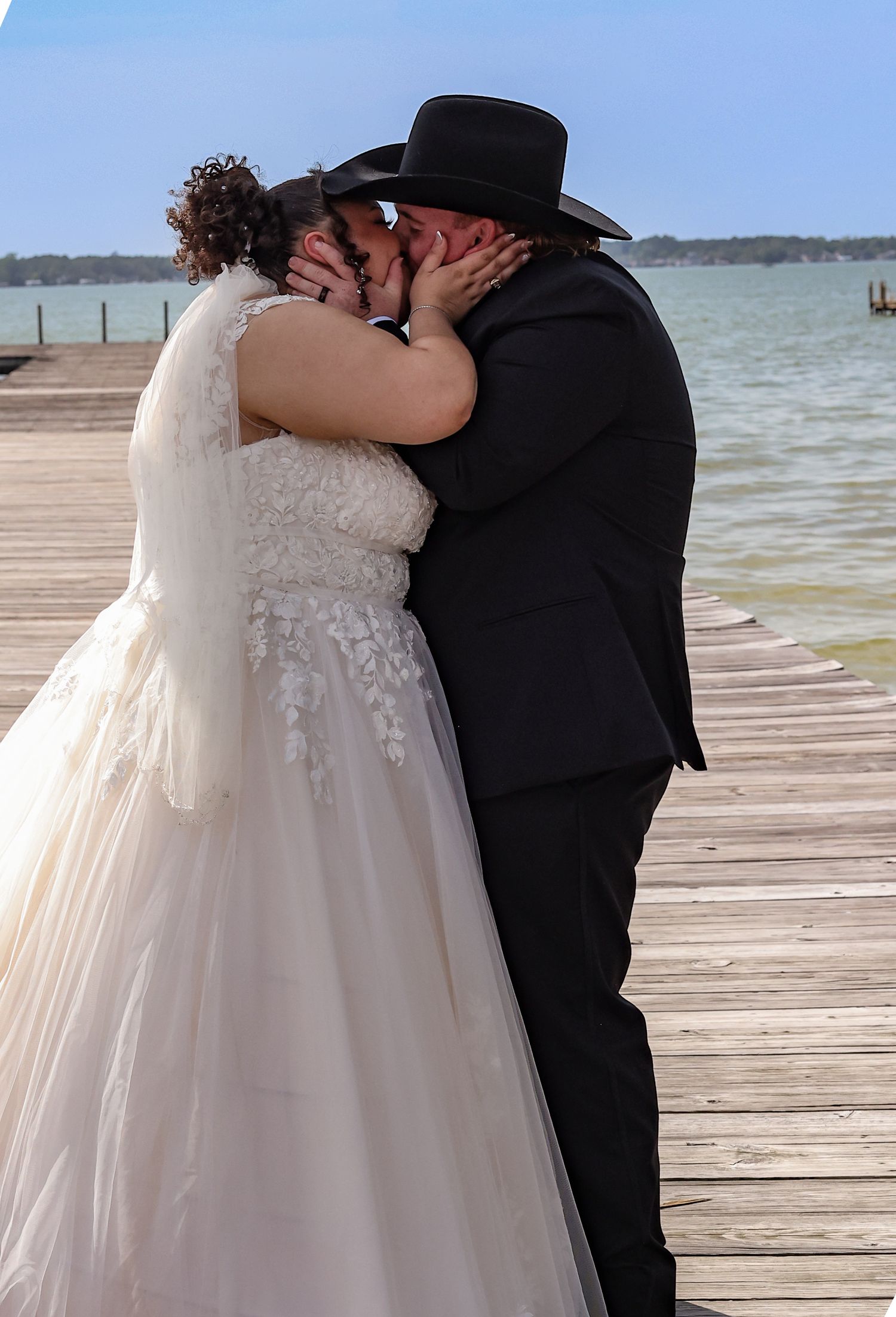 Romantic moment between newlyweds on a wooden dock with water and blue sky in background.