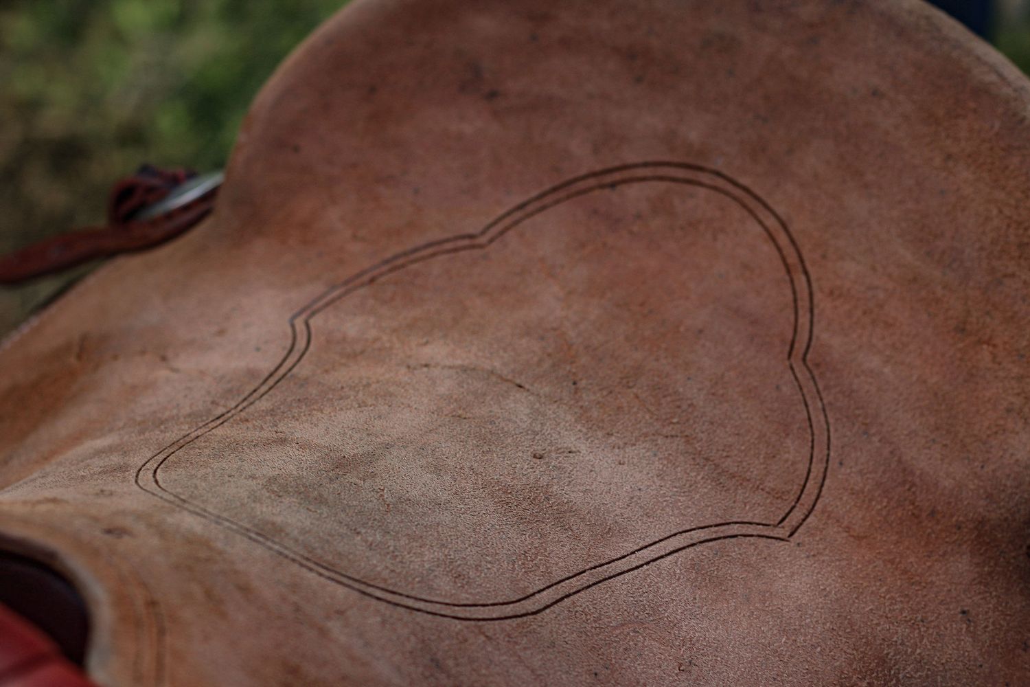 Detailed view of a heart-shaped design tooled into brown leather saddle.