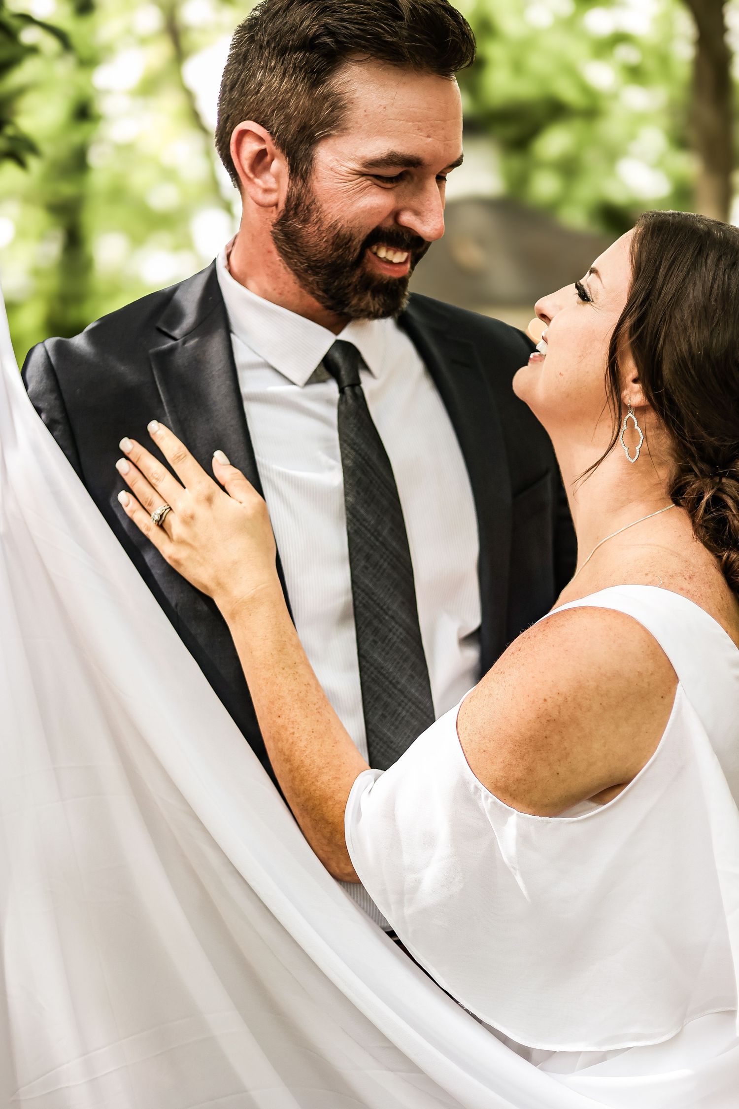 A romantic couple in wedding attire share a joyful moment against a blurred green outdoor background.