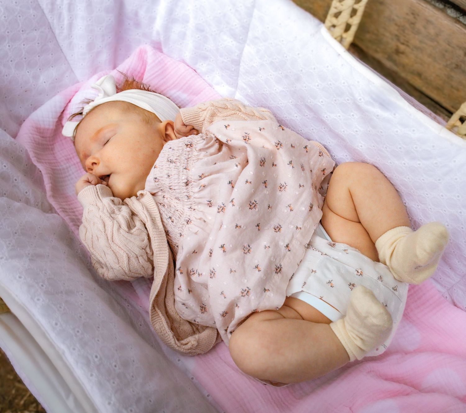 Peaceful newborn baby resting on pink blanket wearing floral printed outfit.
