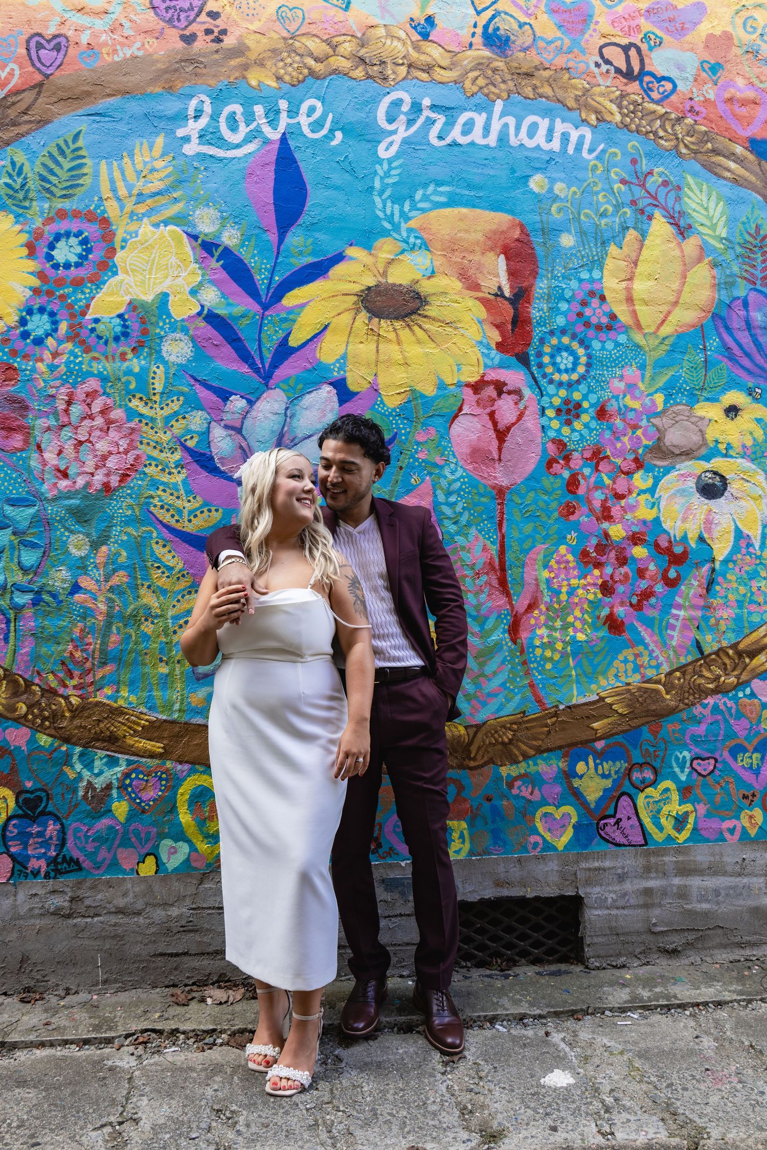 A couple embracing against a backdrop of a colorful sunflower and floral mural.