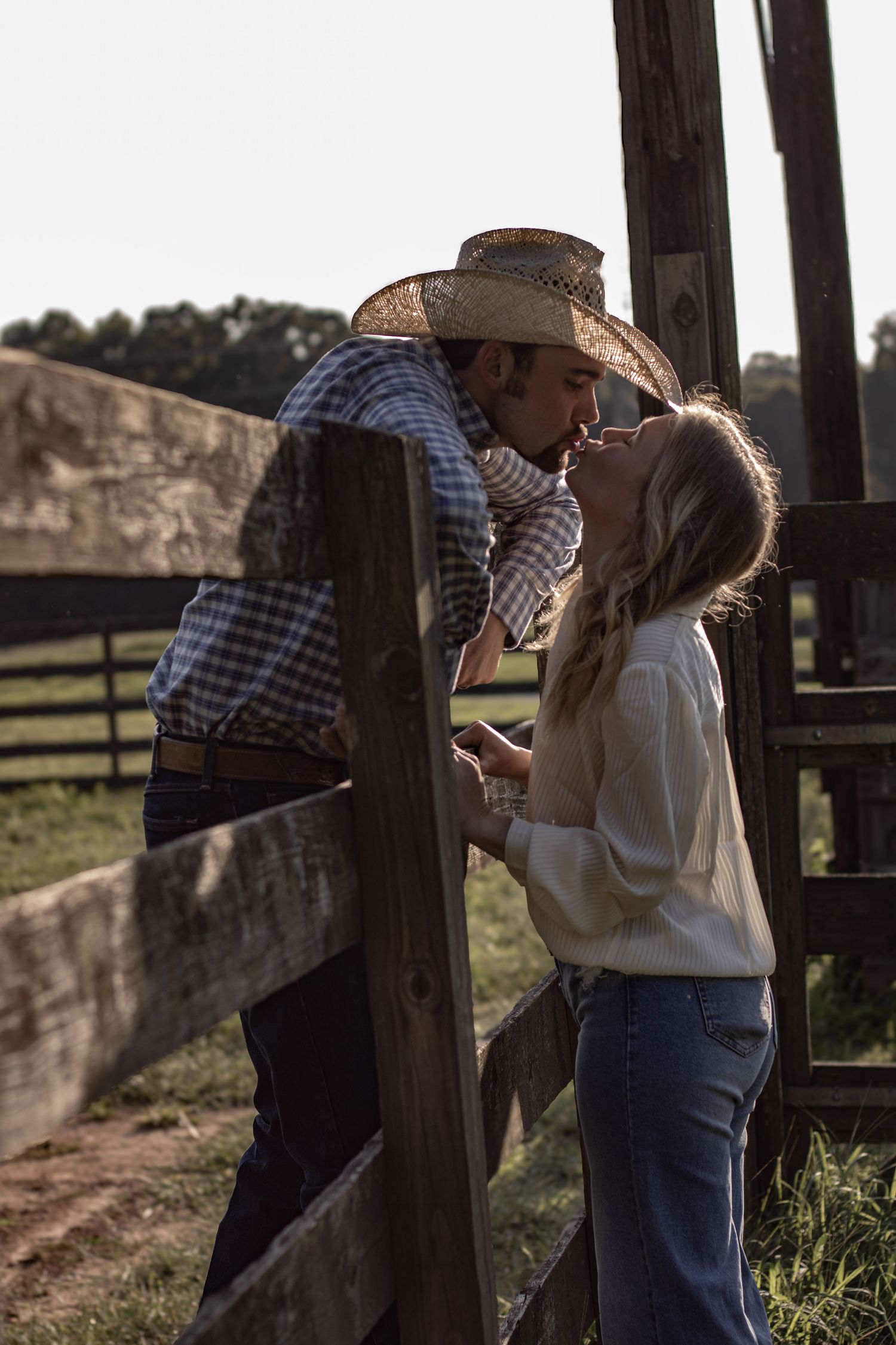 Romantic couple sharing tender moments by a rustic wooden fence at golden hour.
