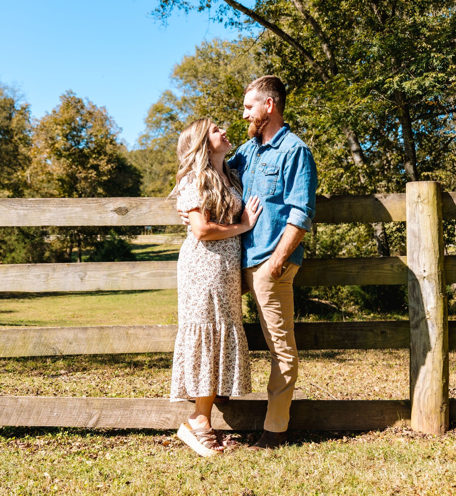 Couple sharing intimate moments along a wooden fence in autumn sunlight.