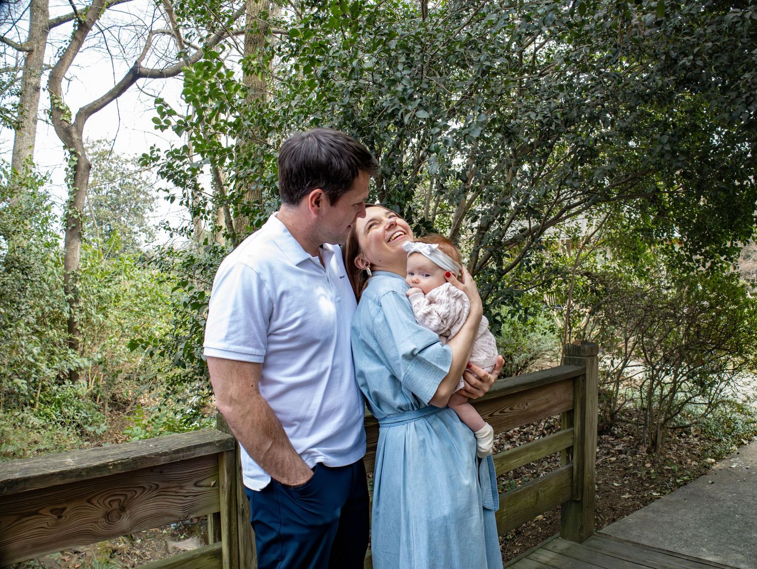 A tender family moment captured on a wooden walkway surrounded by greenery.