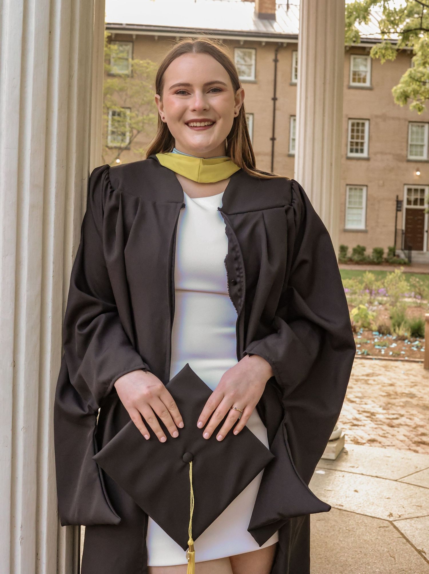 Graduate poses between classical columns wearing traditional academic regalia.