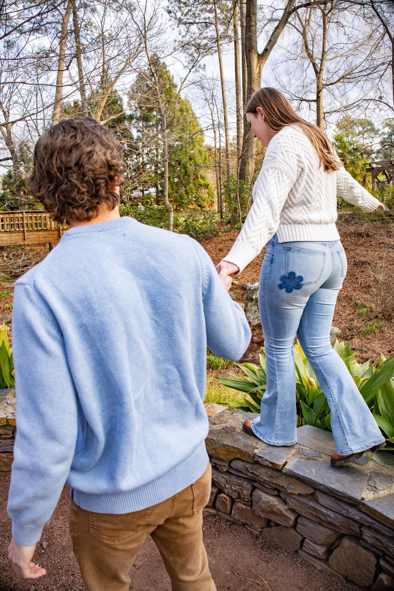 Couple holding hands while walking on stone path in garden.